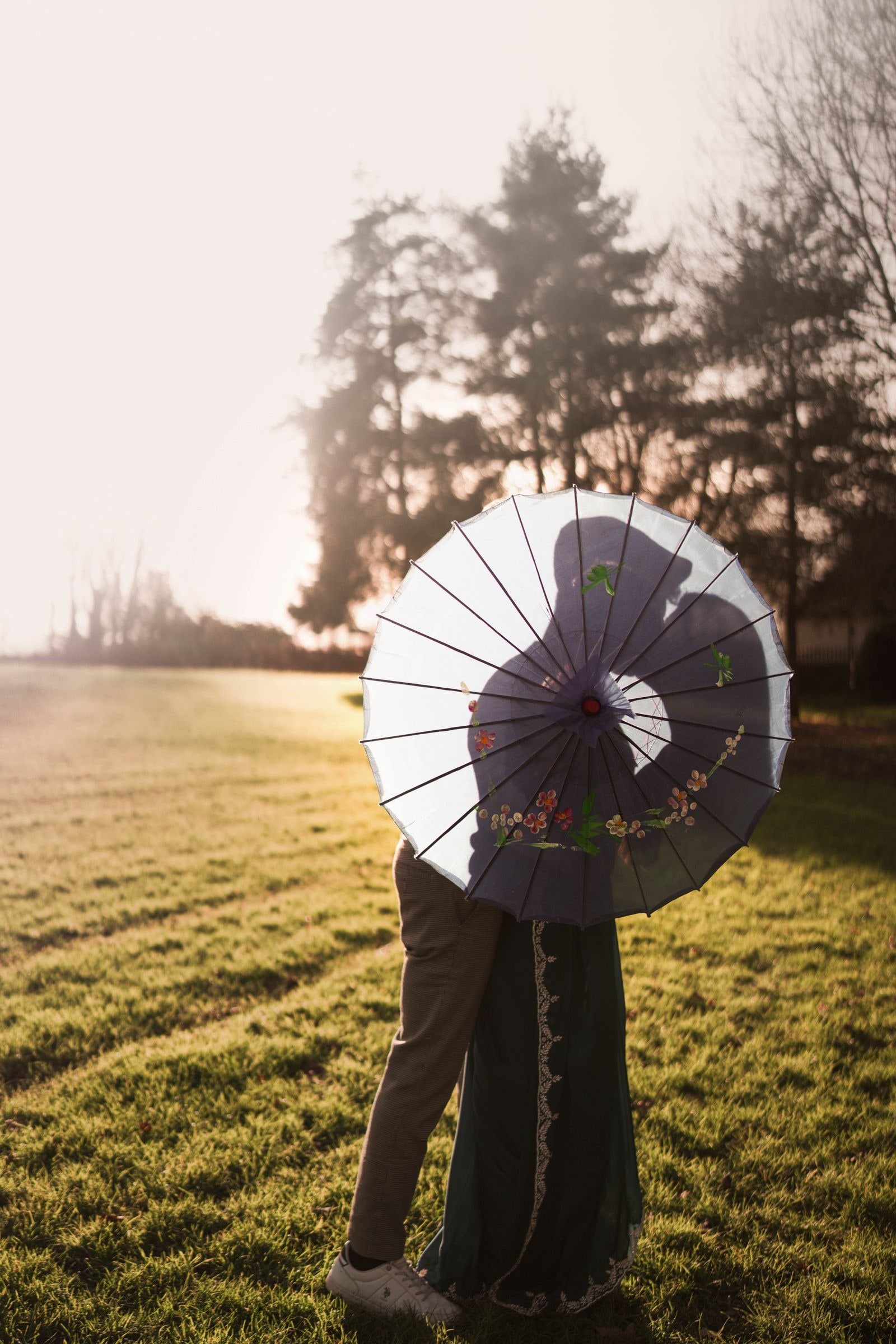 Couple hidden behind a painted parasol in a field at sunrise