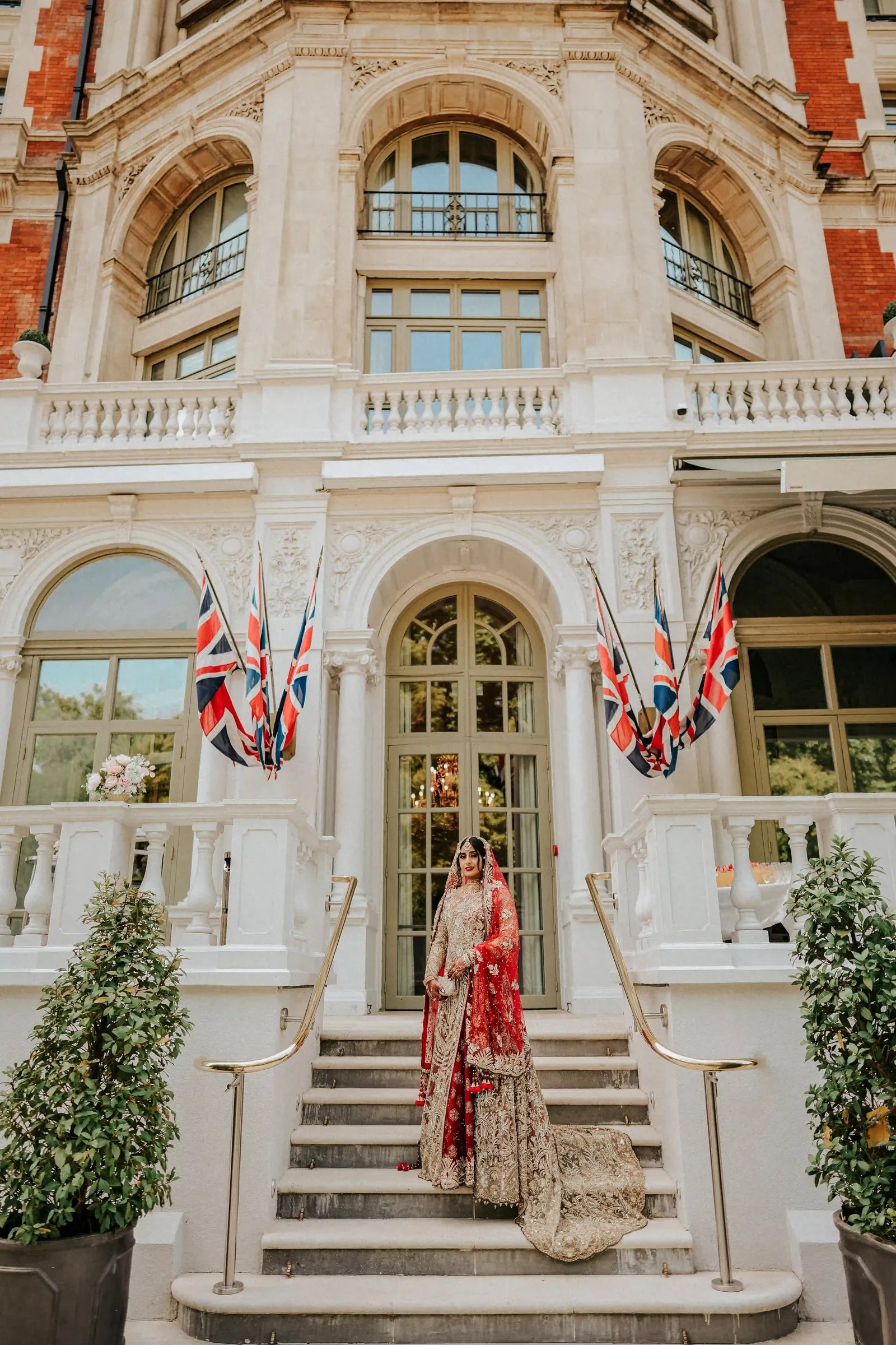 Bride alone on the hotel steps between Union flags, her train falling down the stone
