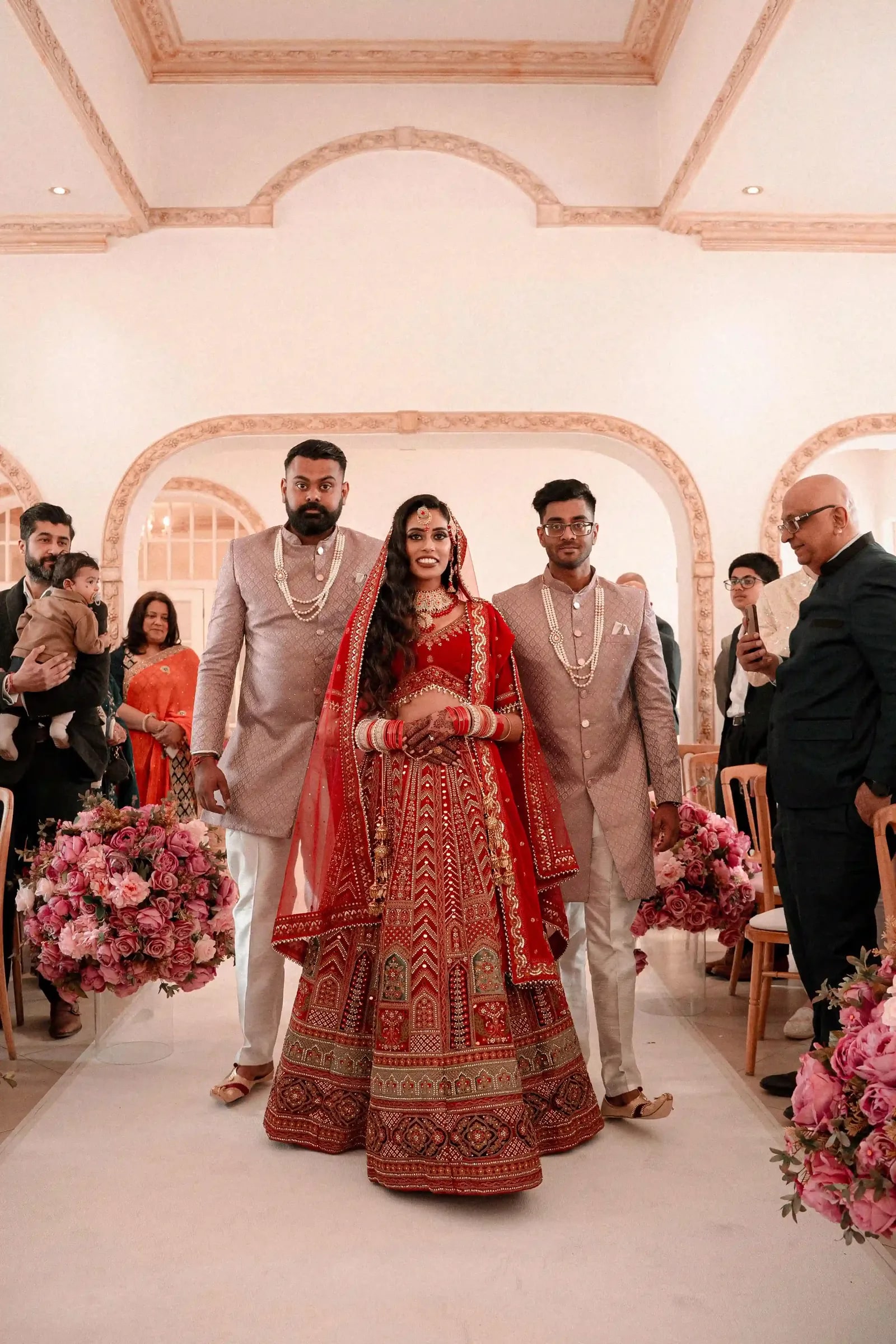 Bride walked down the aisle in a red lehenga by two men in blush sherwanis