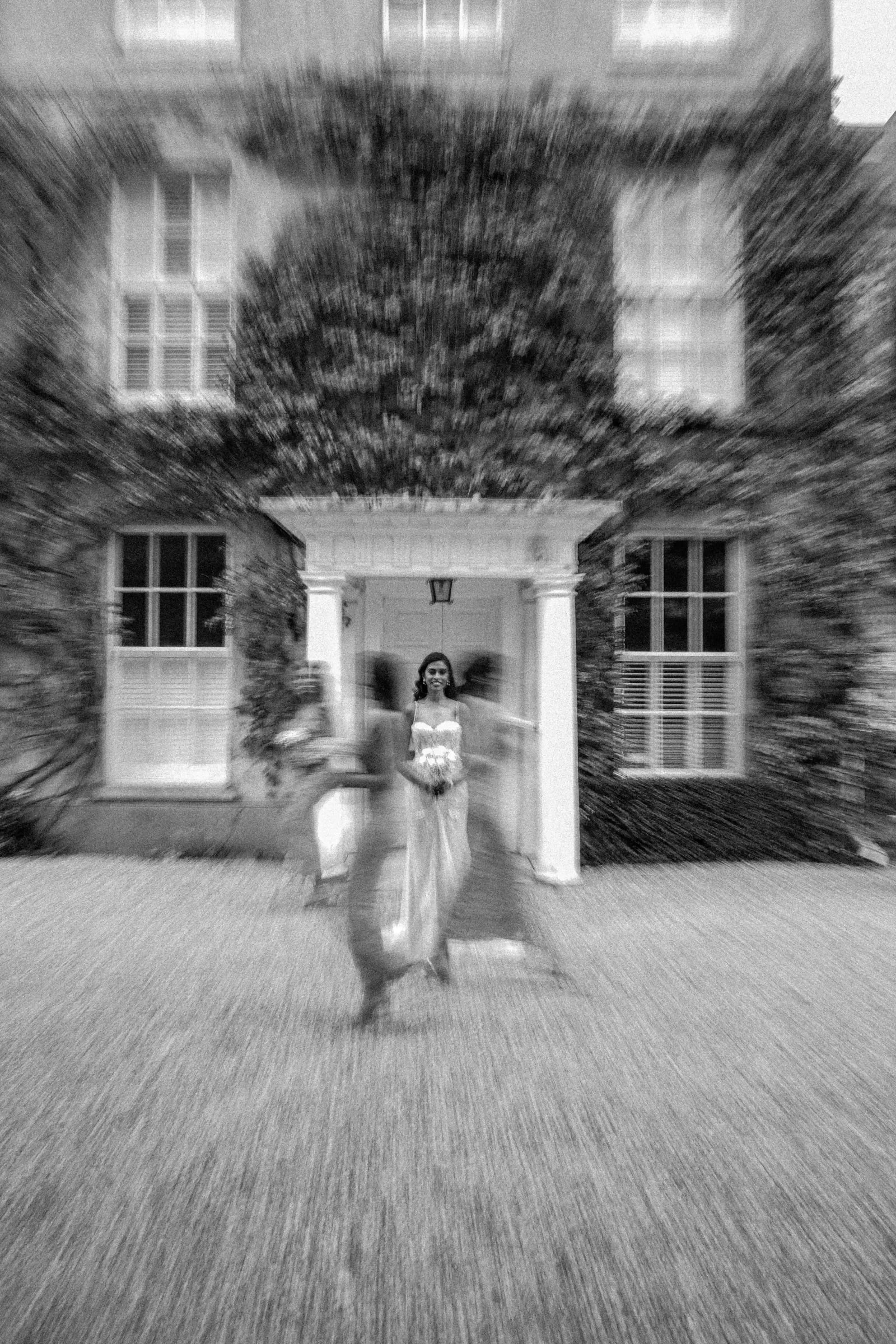 Bride running towards the camera outside the house, blurred with motion, in black and white