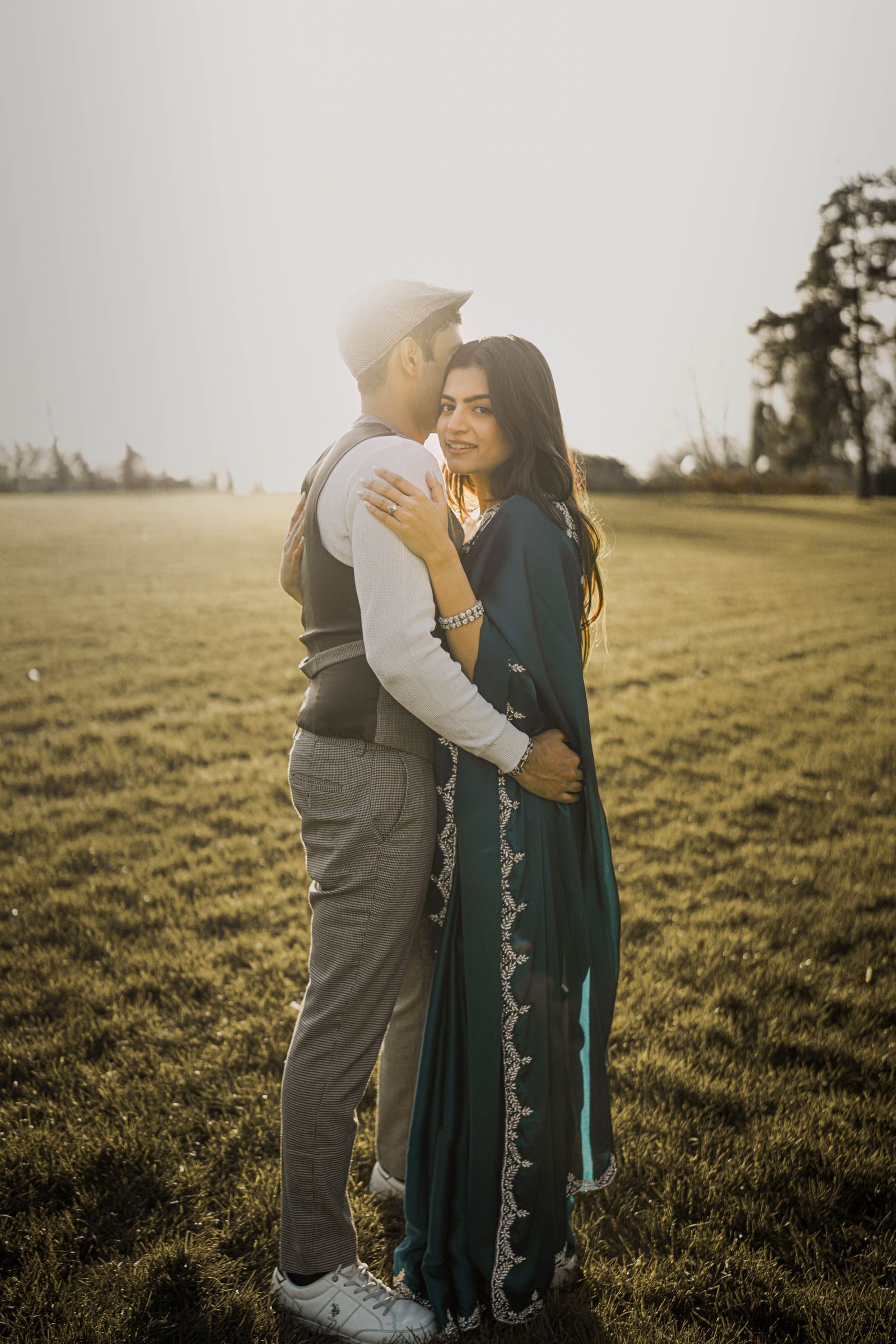 Couple holding each other in an open field, she in a teal sari, he in a flat cap
