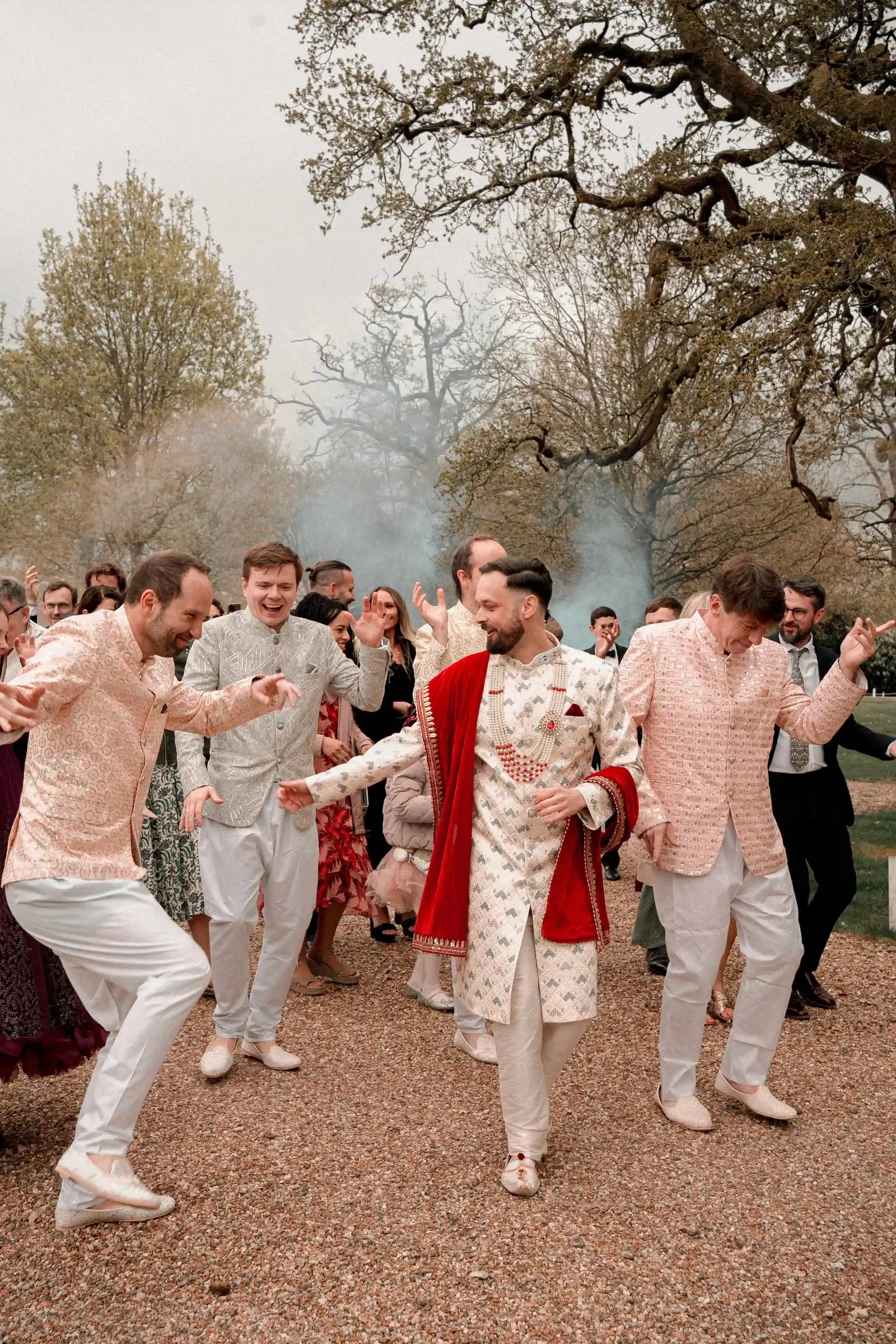 Groom in ivory and red dancing in with his friends during the baraat