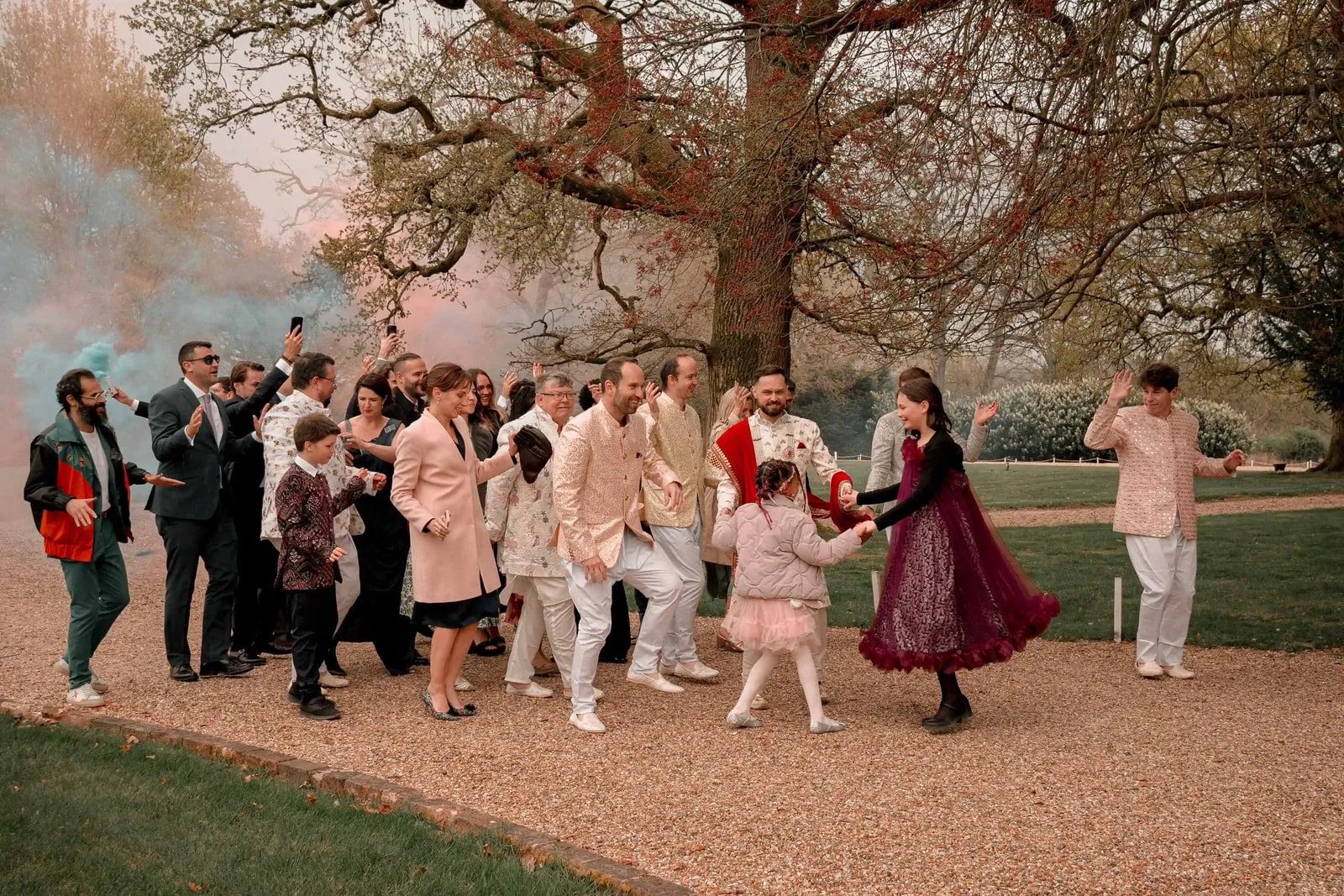 The baraat crossing the lawn with coloured smoke drifting through the trees