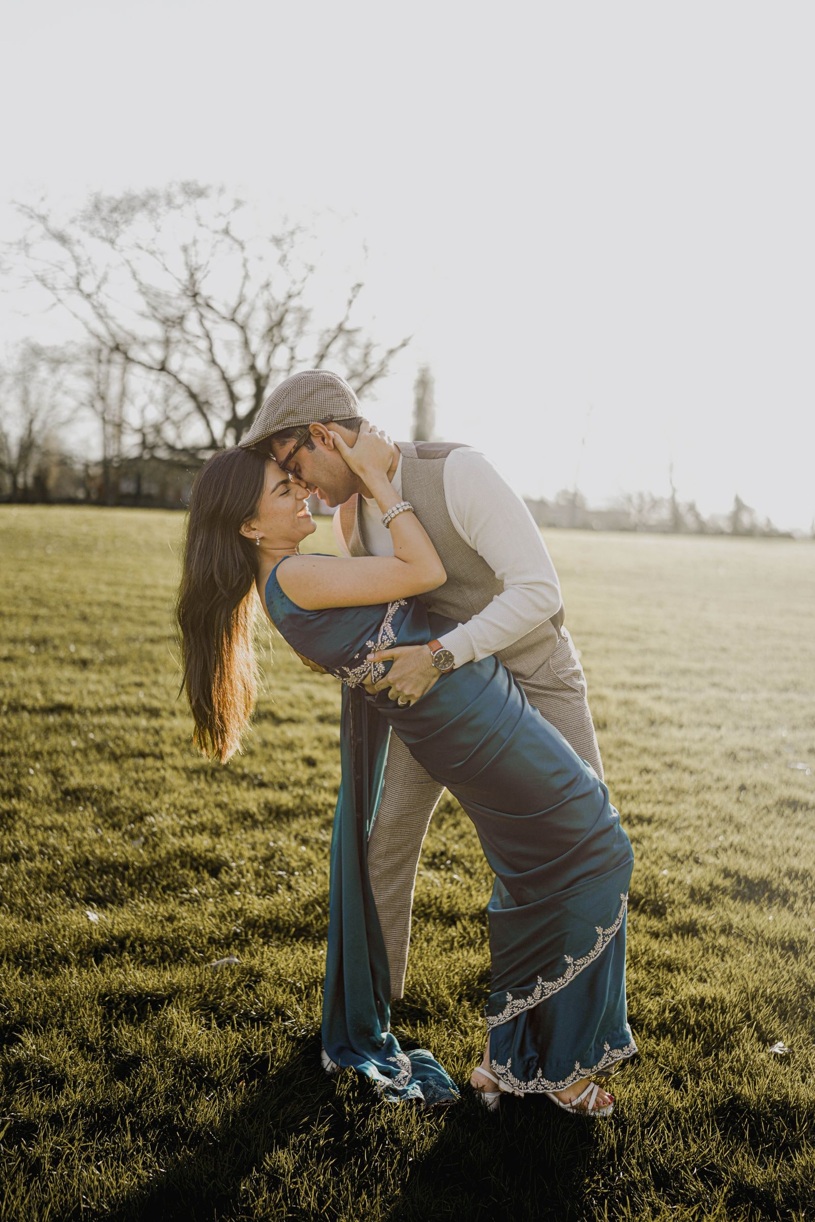 Groom to be dipping his fiancee in the field, bare trees behind them