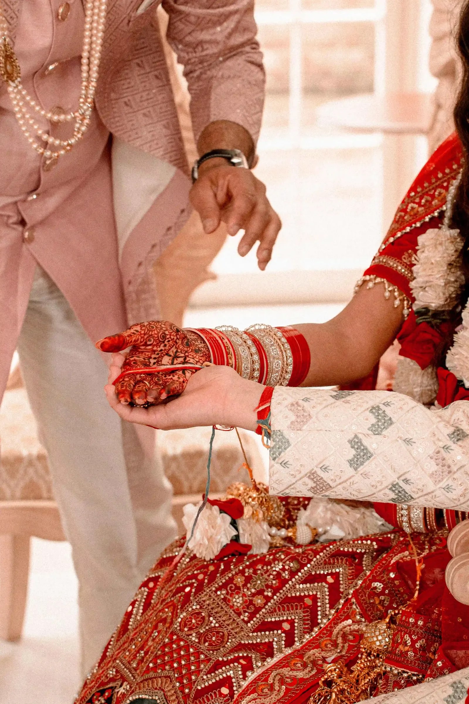 Hands joined over the ceremonial offering, the bride's hennaed and full of bangles