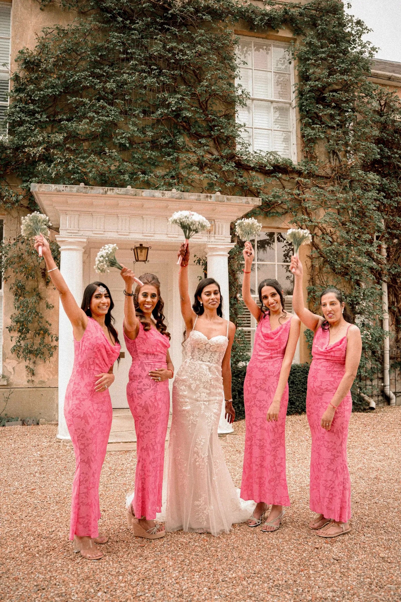Bridesmaids raising their bouquets around the bride outside the house