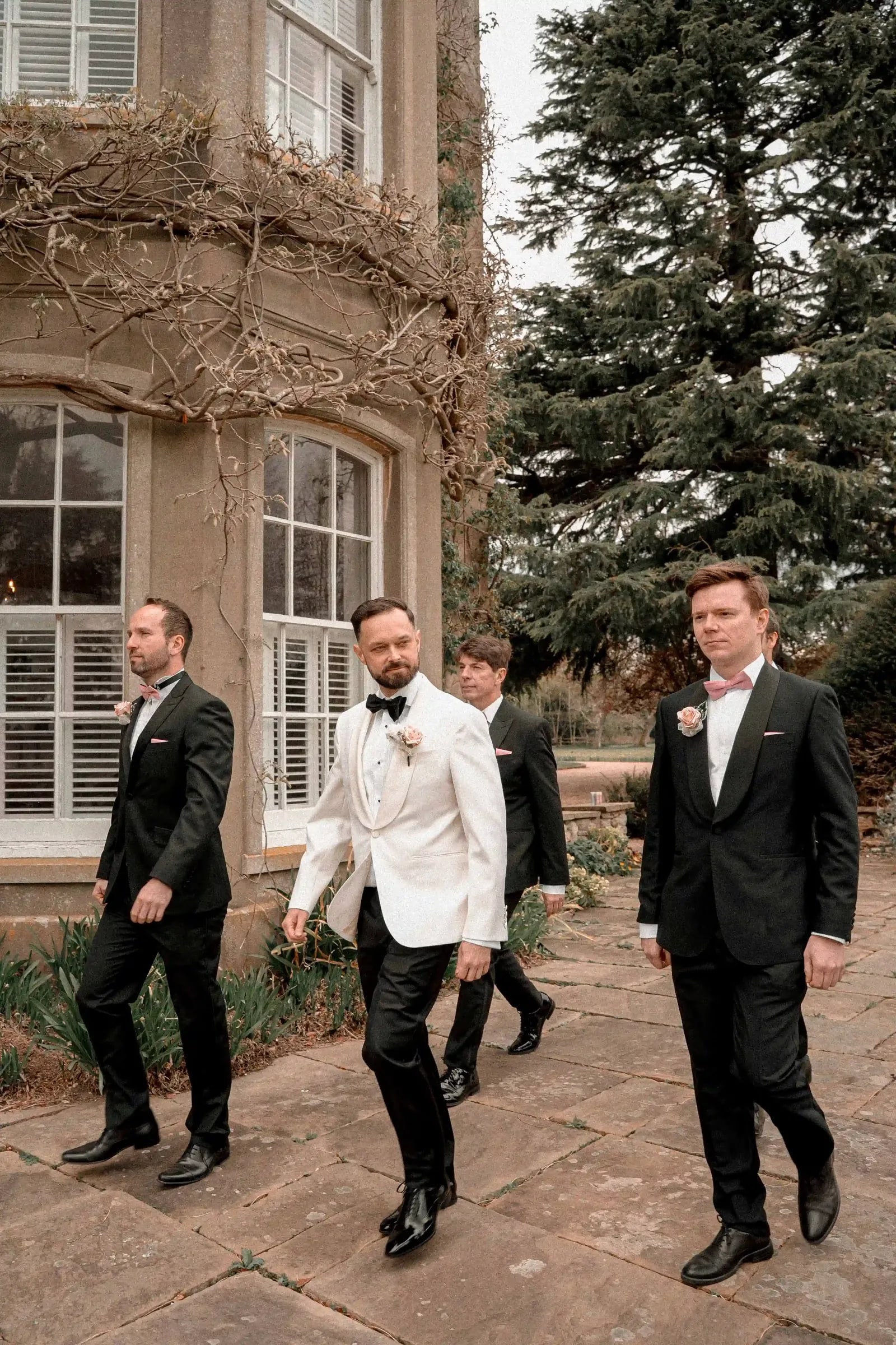 Groom in a white dinner jacket walking with his groomsmen along the terrace
