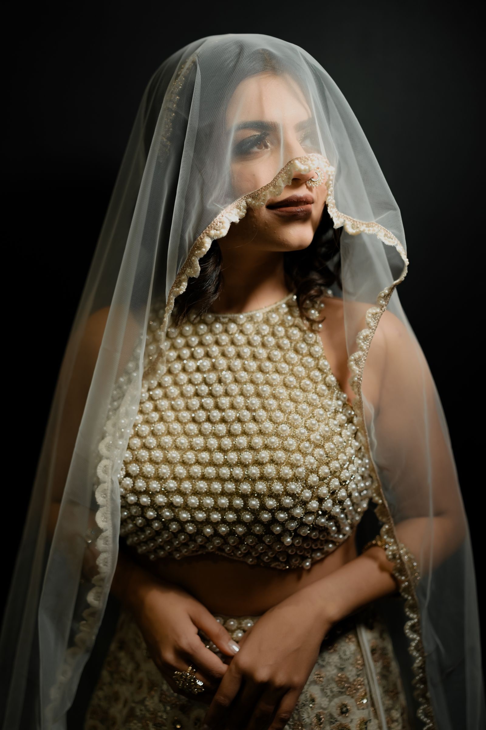Bride lit against a dark background in a pearl-covered blouse and sheer veil