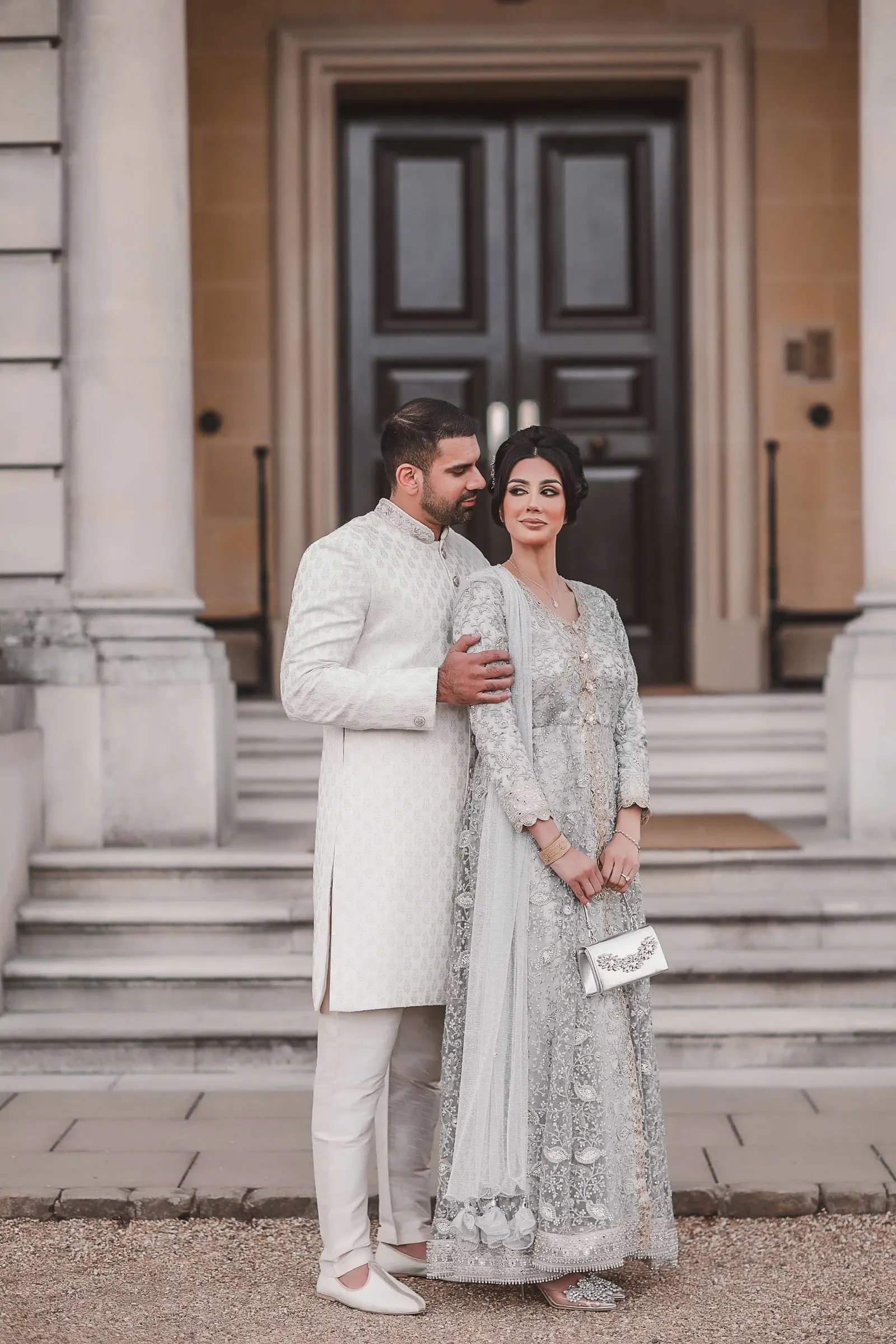 Couple in matching ivory and silver outfits at the doorway of the house