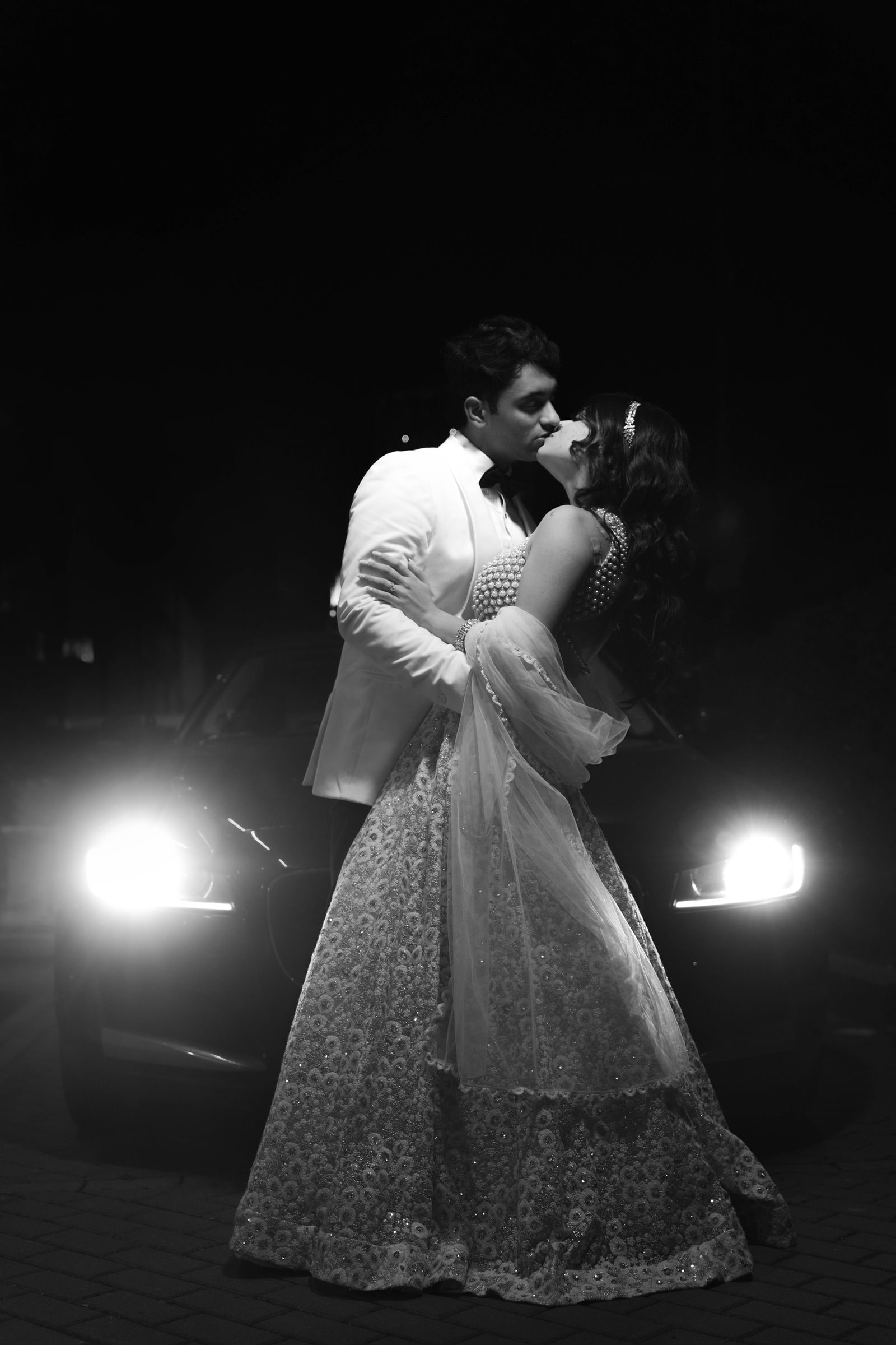 Couple embracing in front of car headlights at night, in black and white