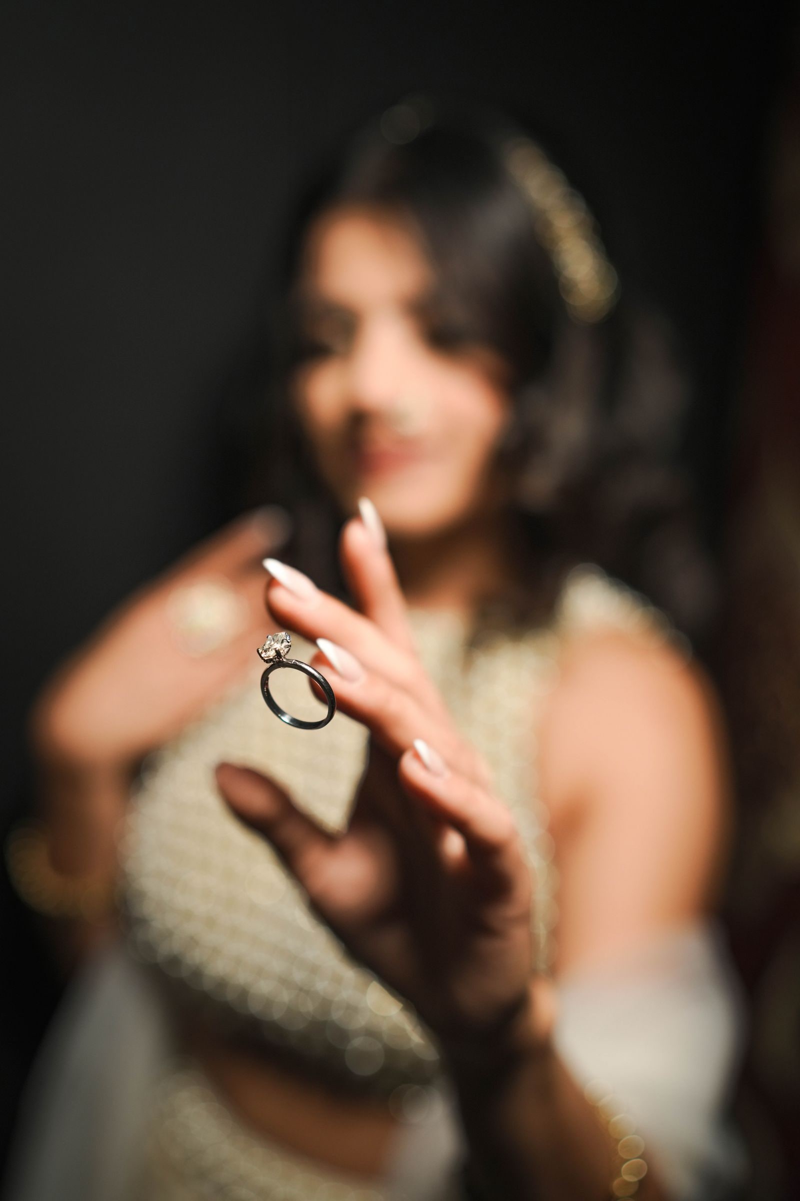 The engagement ring held up in focus, the bride soft behind it