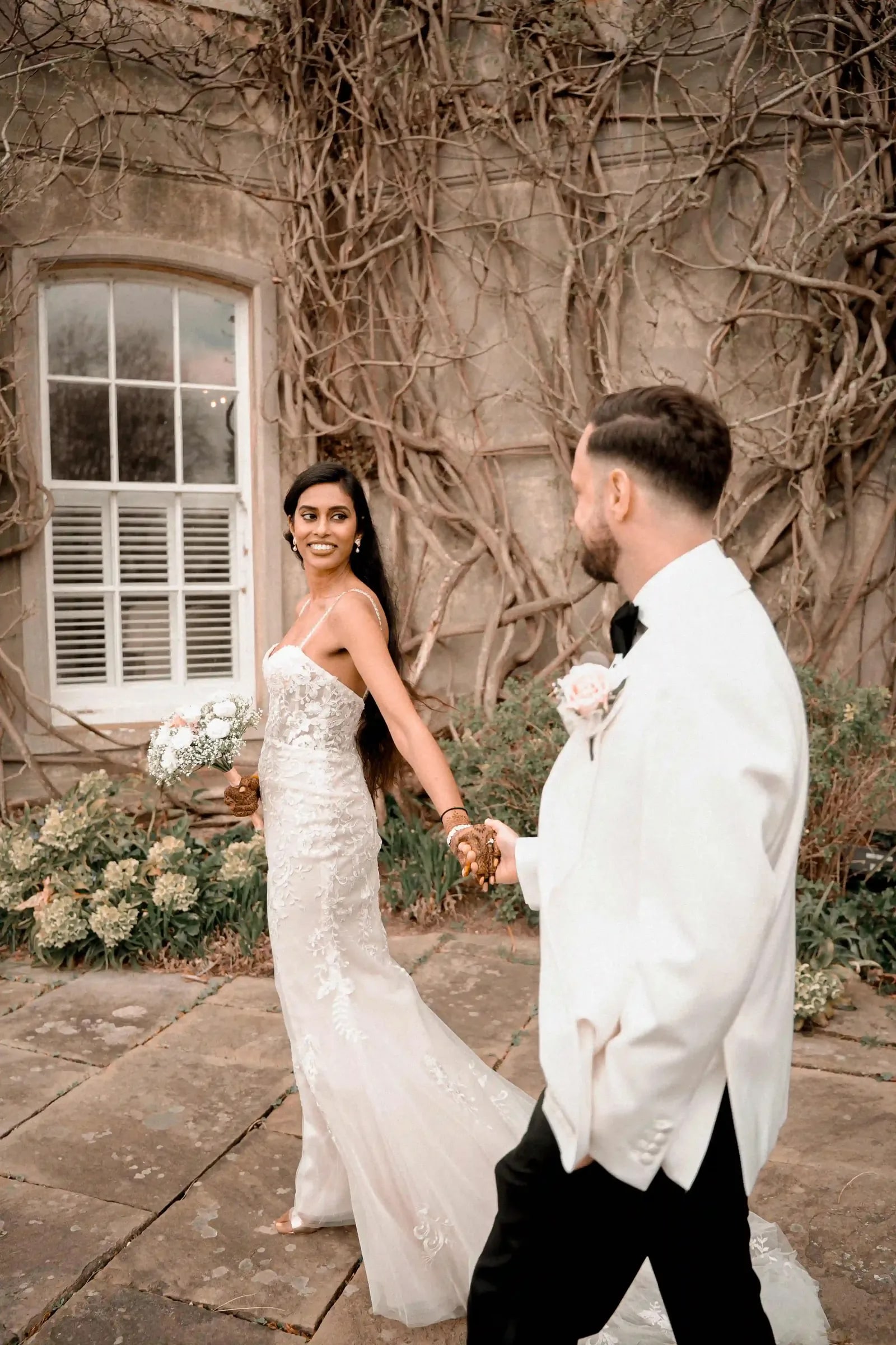 Bride leading her groom by the hand along the terrace, both looking back