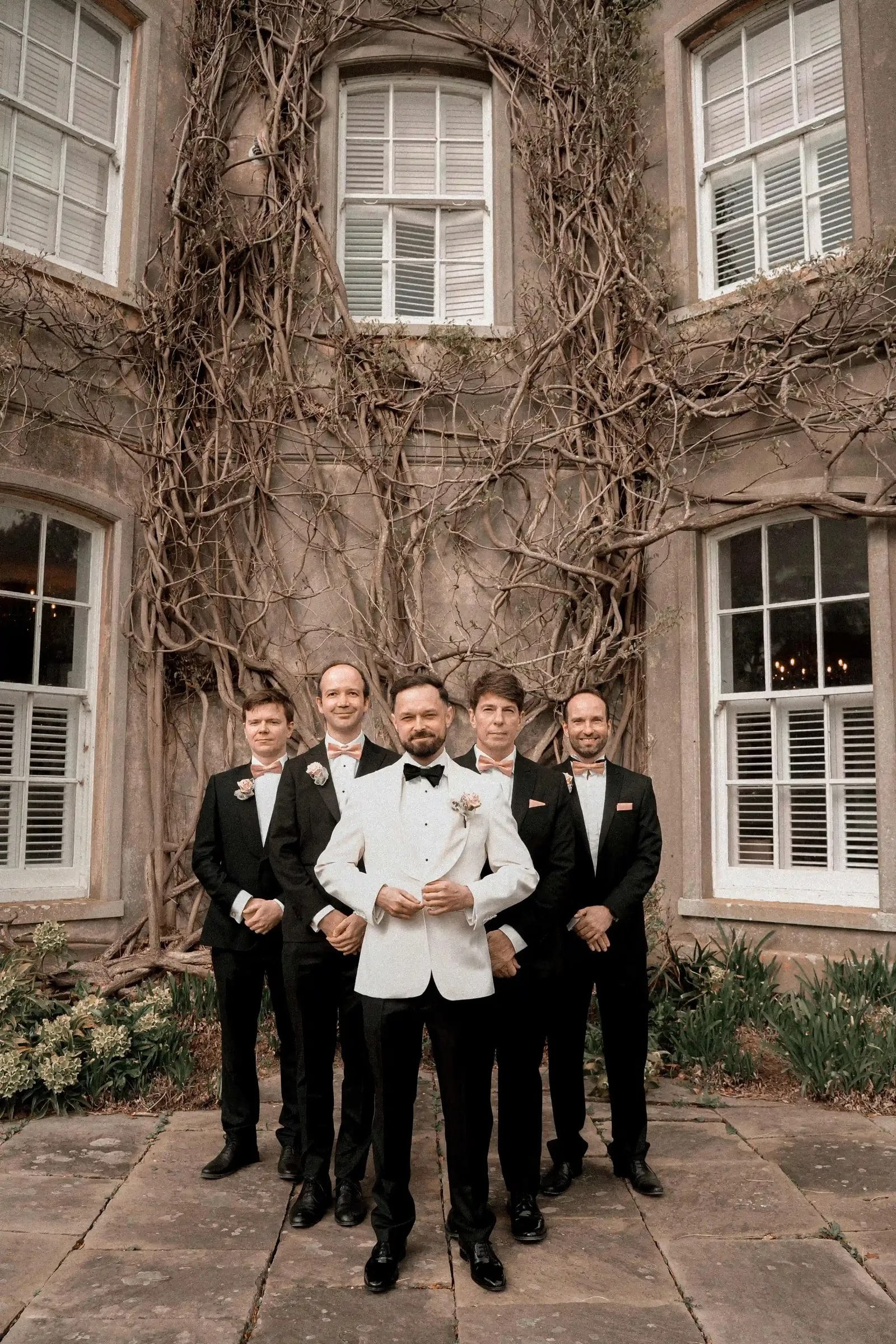 Groom in a white dinner jacket with his groomsmen in black tie on the terrace