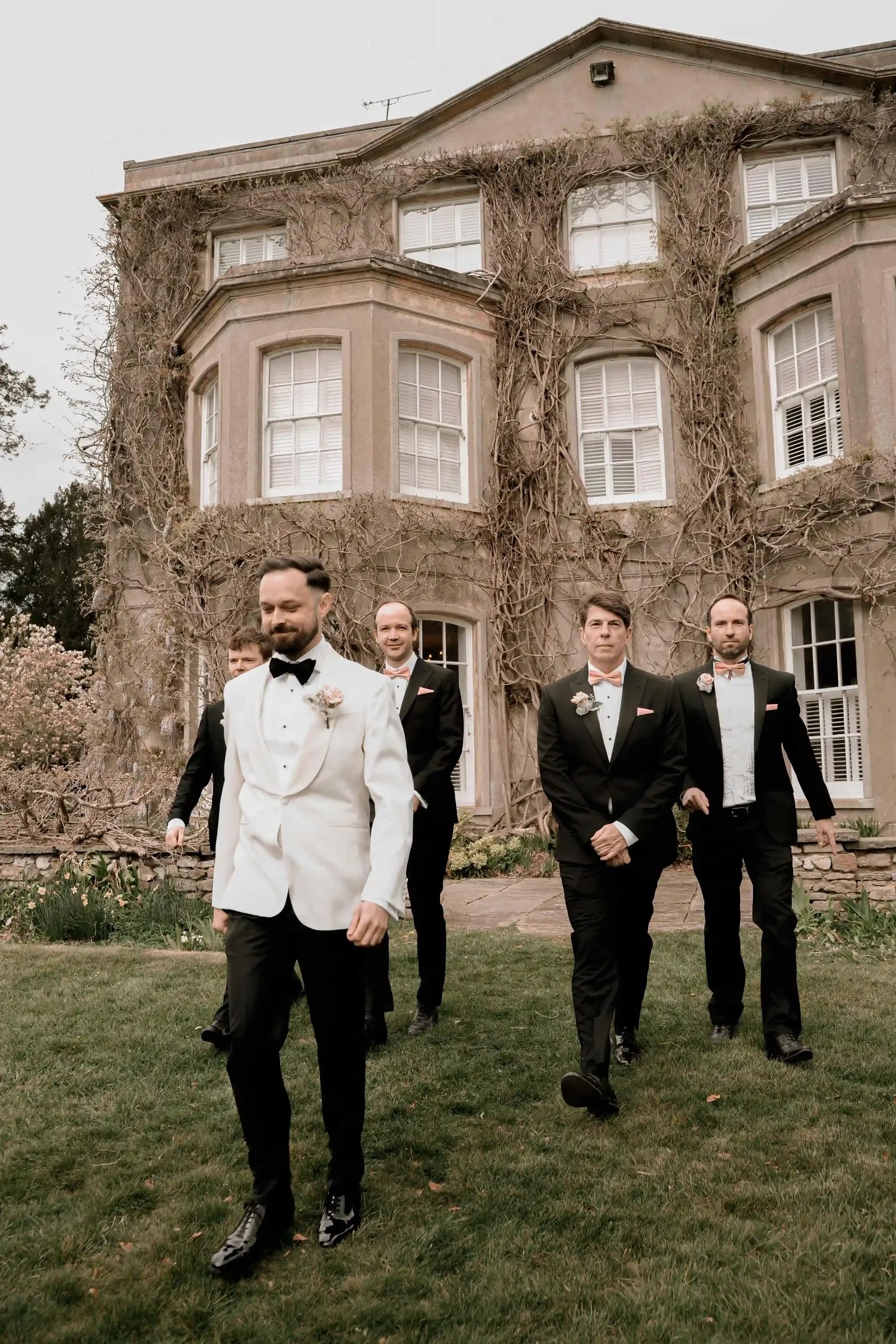Groom and groomsmen walking across the lawn towards the camera