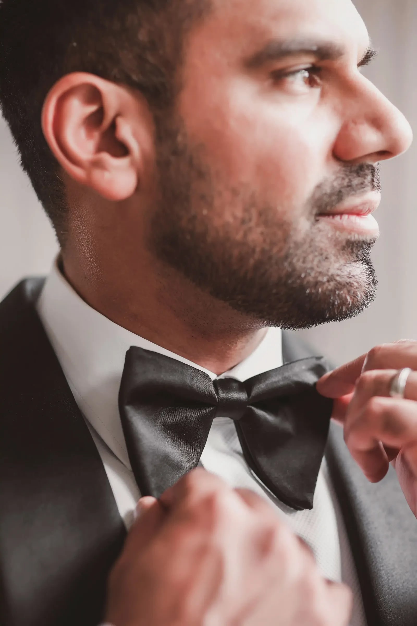 Close portrait of the groom fastening his bow tie in profile