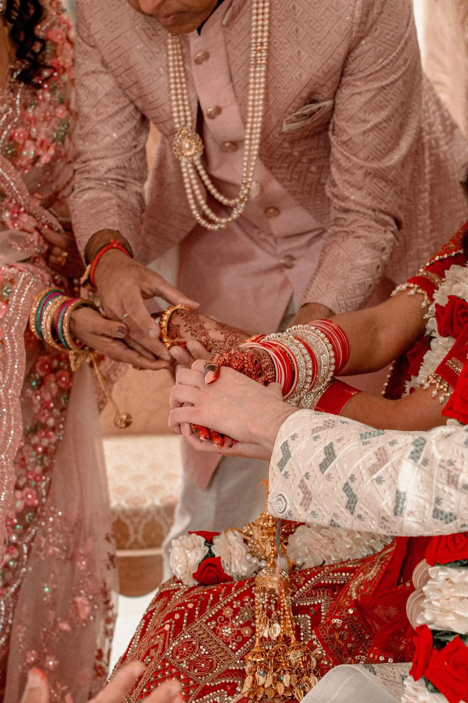 Close view of hands during the ceremony, the bride's wrists stacked with red and gold bangles
