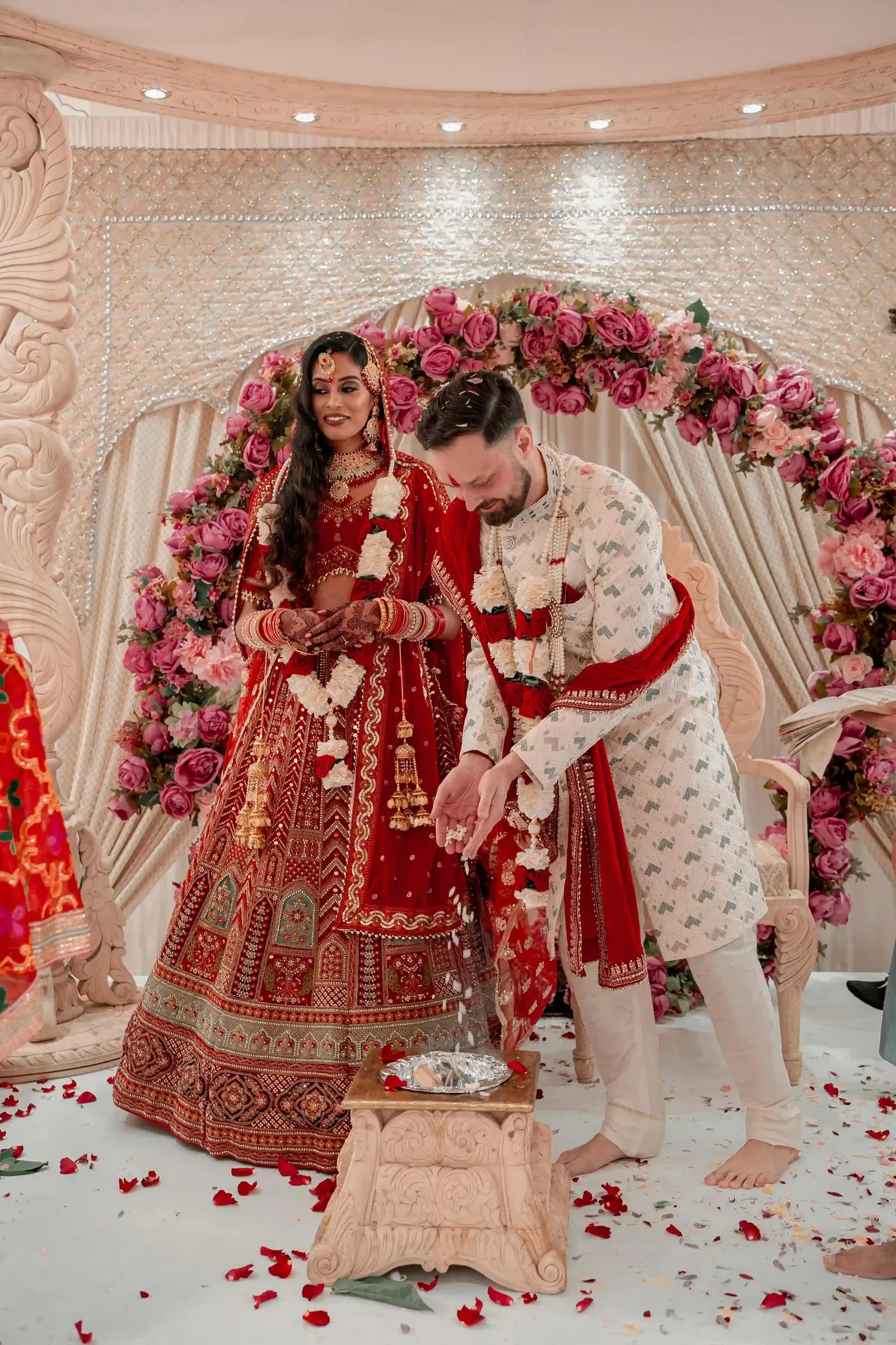 Bride and groom during the ceremony beneath a pink flowered arch, petals scattered at their feet