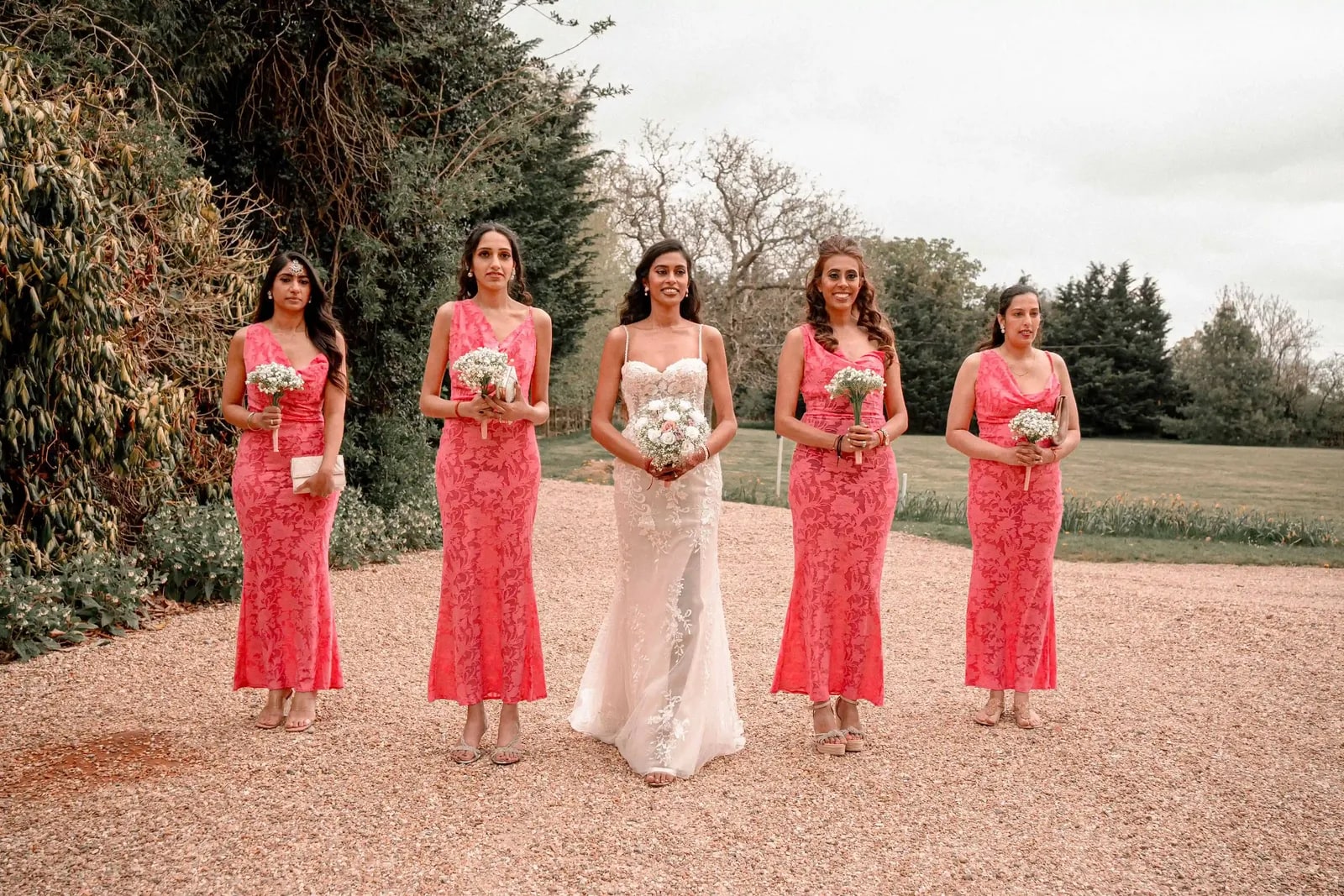 Bride and bridesmaids in a line on the drive, each holding white flowers