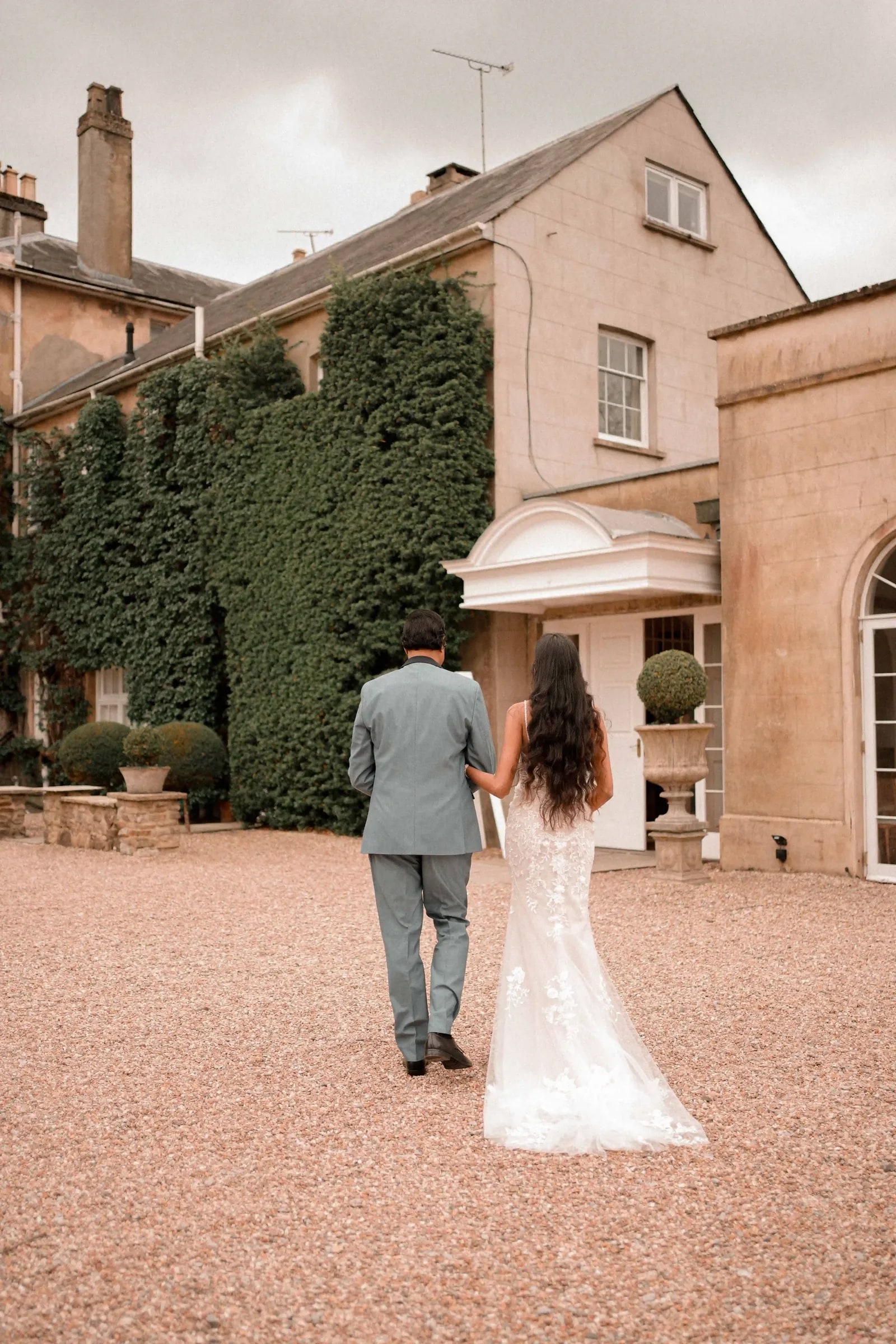 Bride and groom walking away towards the house, seen from behind