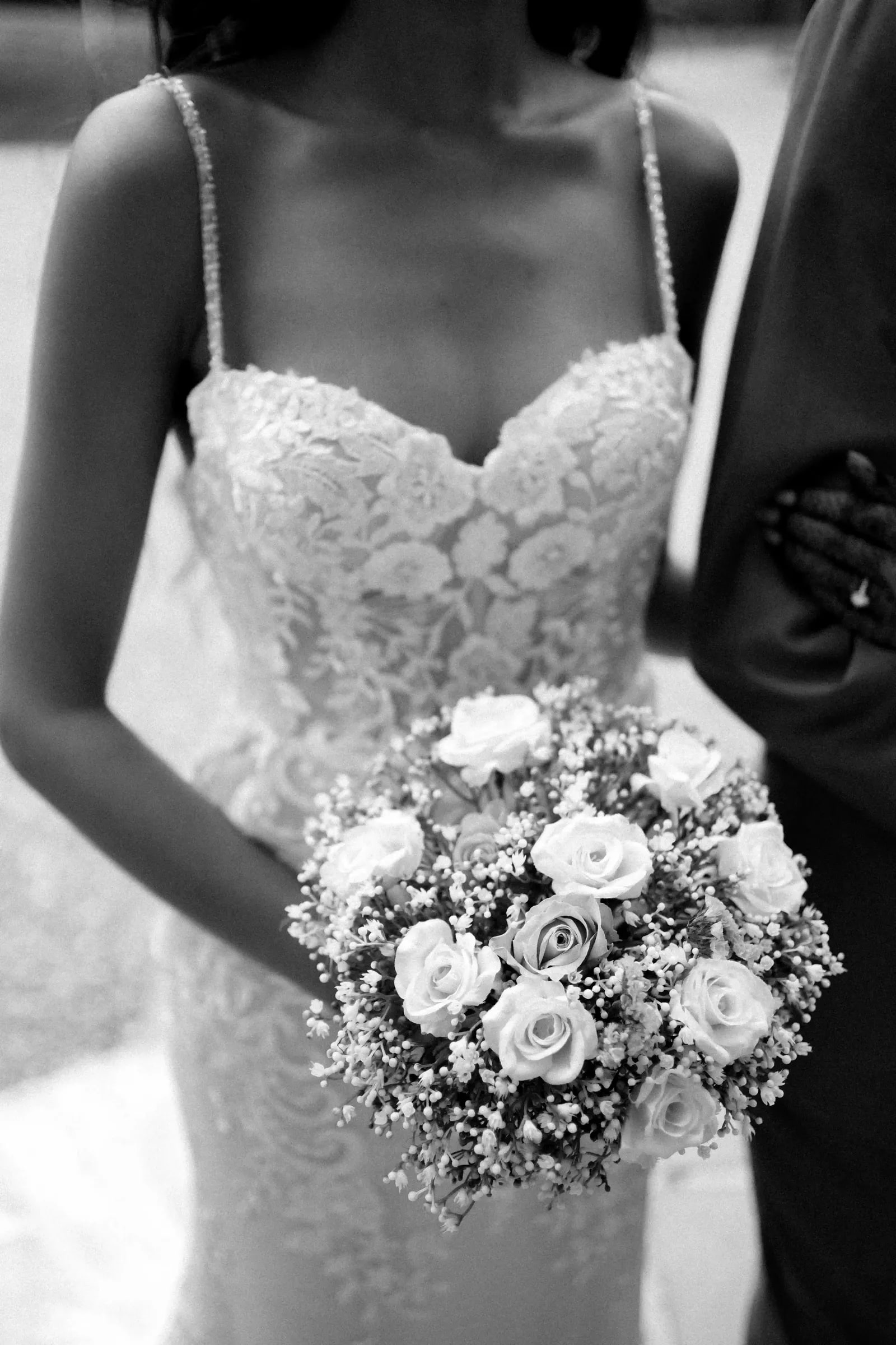 Bride's white rose bouquet held against her lace gown, in black and white