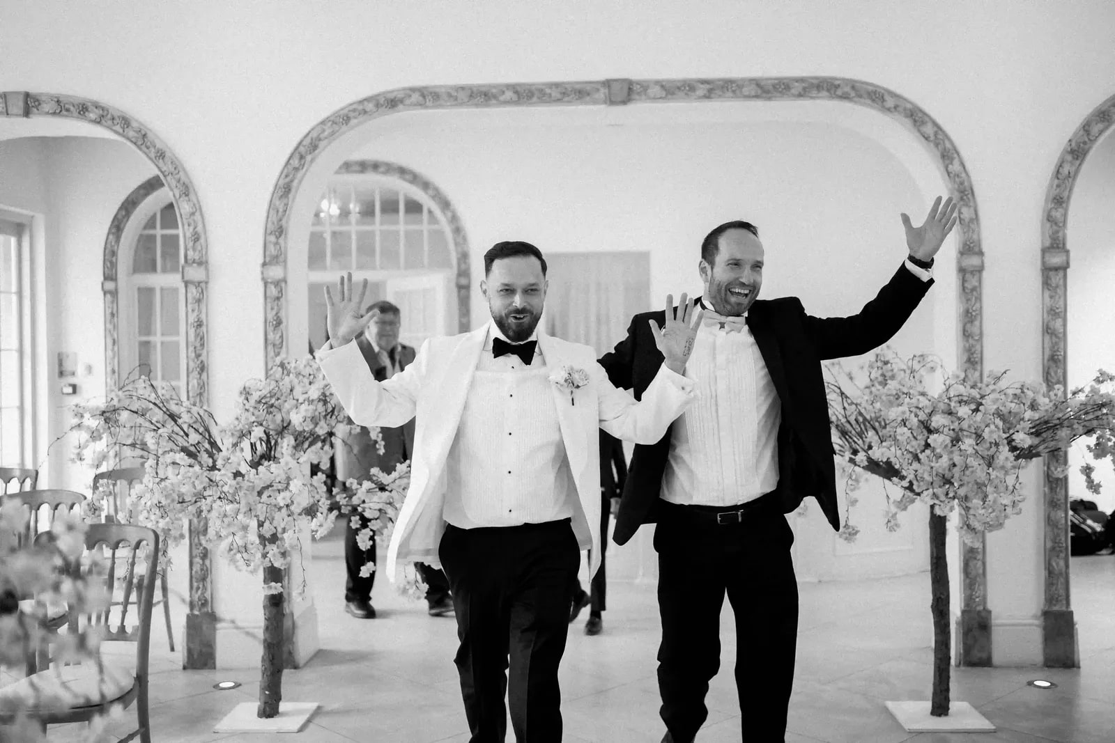 Groom and a friend walking down the aisle with their hands raised, in black and white