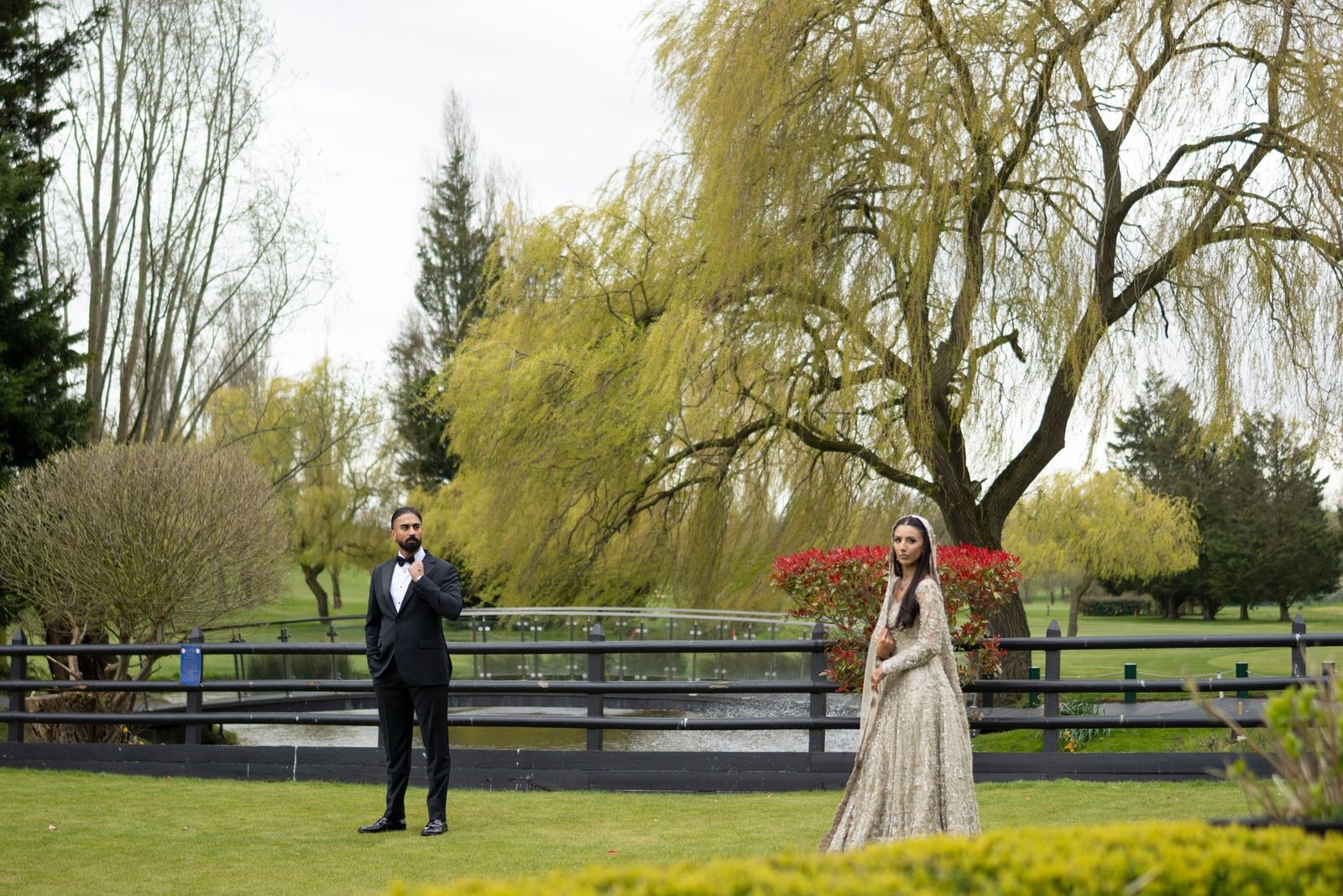 Couple standing apart on the grass beneath a willow by the water