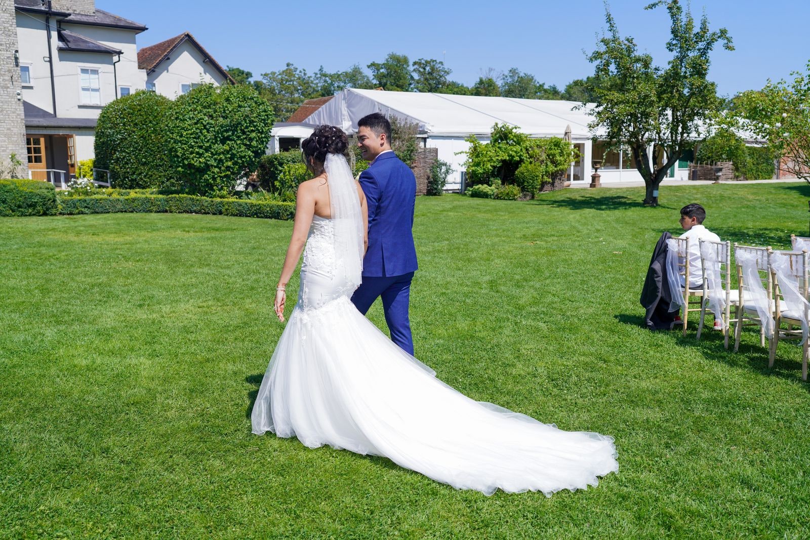 Bride's long train spread across the lawn as she stands with her groom in a blue suit
