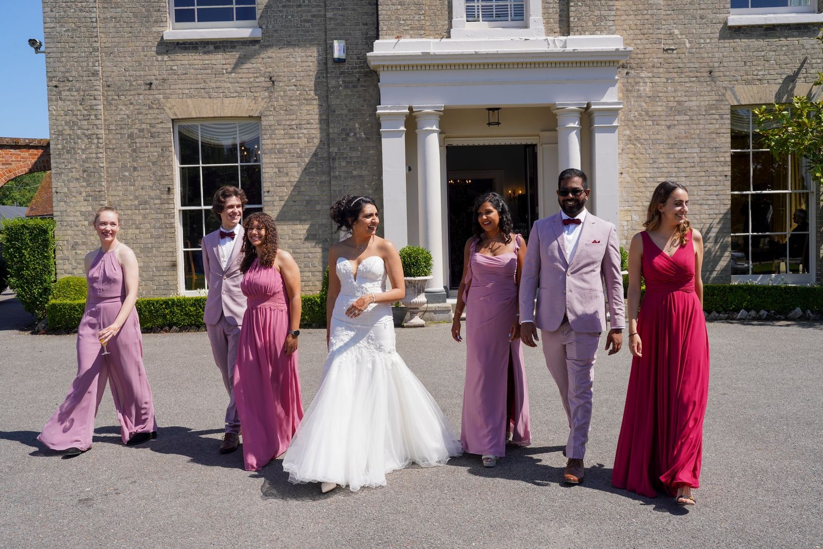 Bride and her bridal party in shades of pink walking out from the house entrance