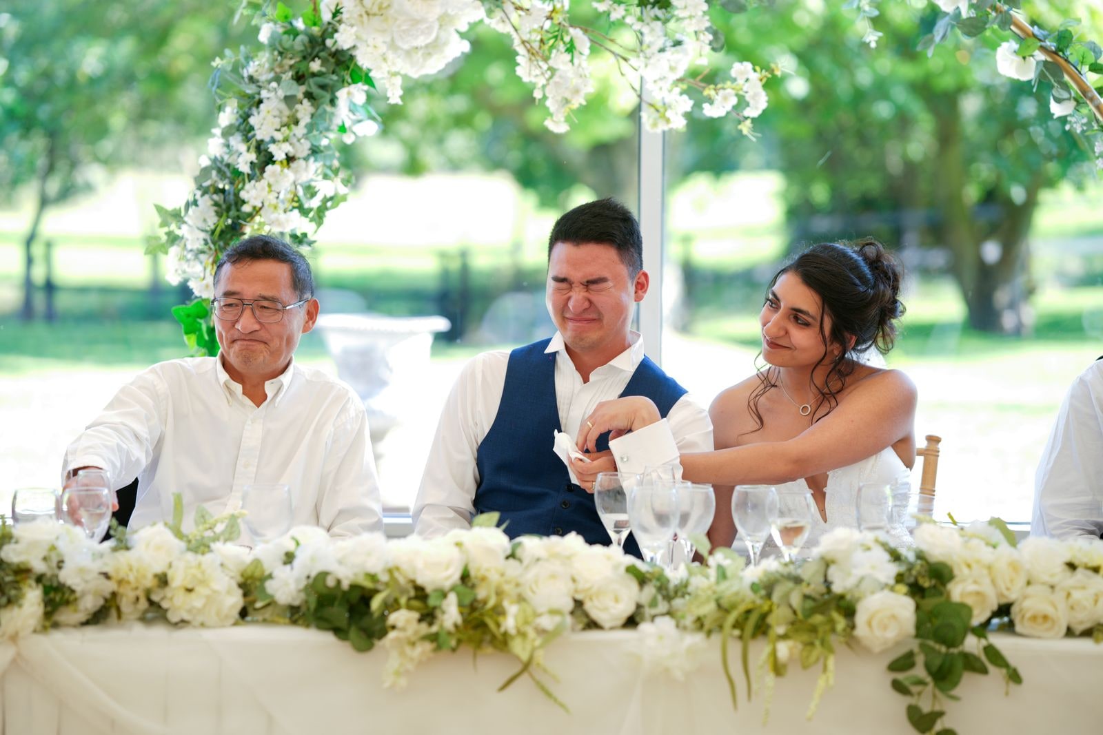 Bride reaching across the top table to her groom during the speeches, guests either side