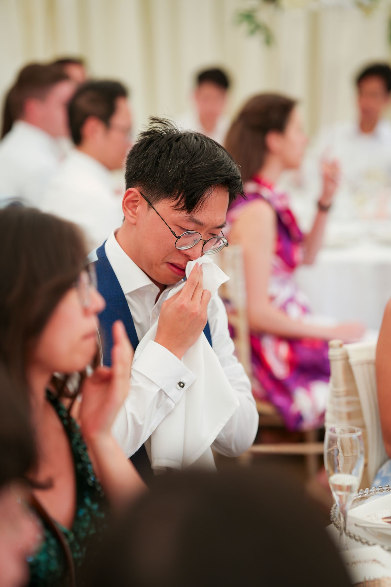 Guest in a blue waistcoat wiping his eyes with a napkin during the speeches