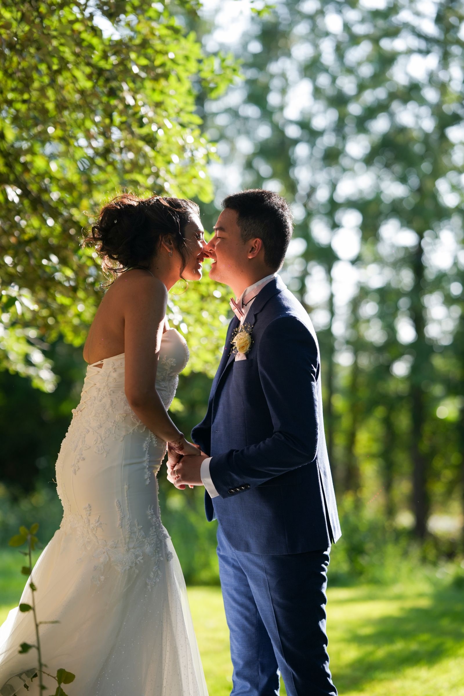 Bride and groom kissing under trees, sunlight coming through the leaves behind them