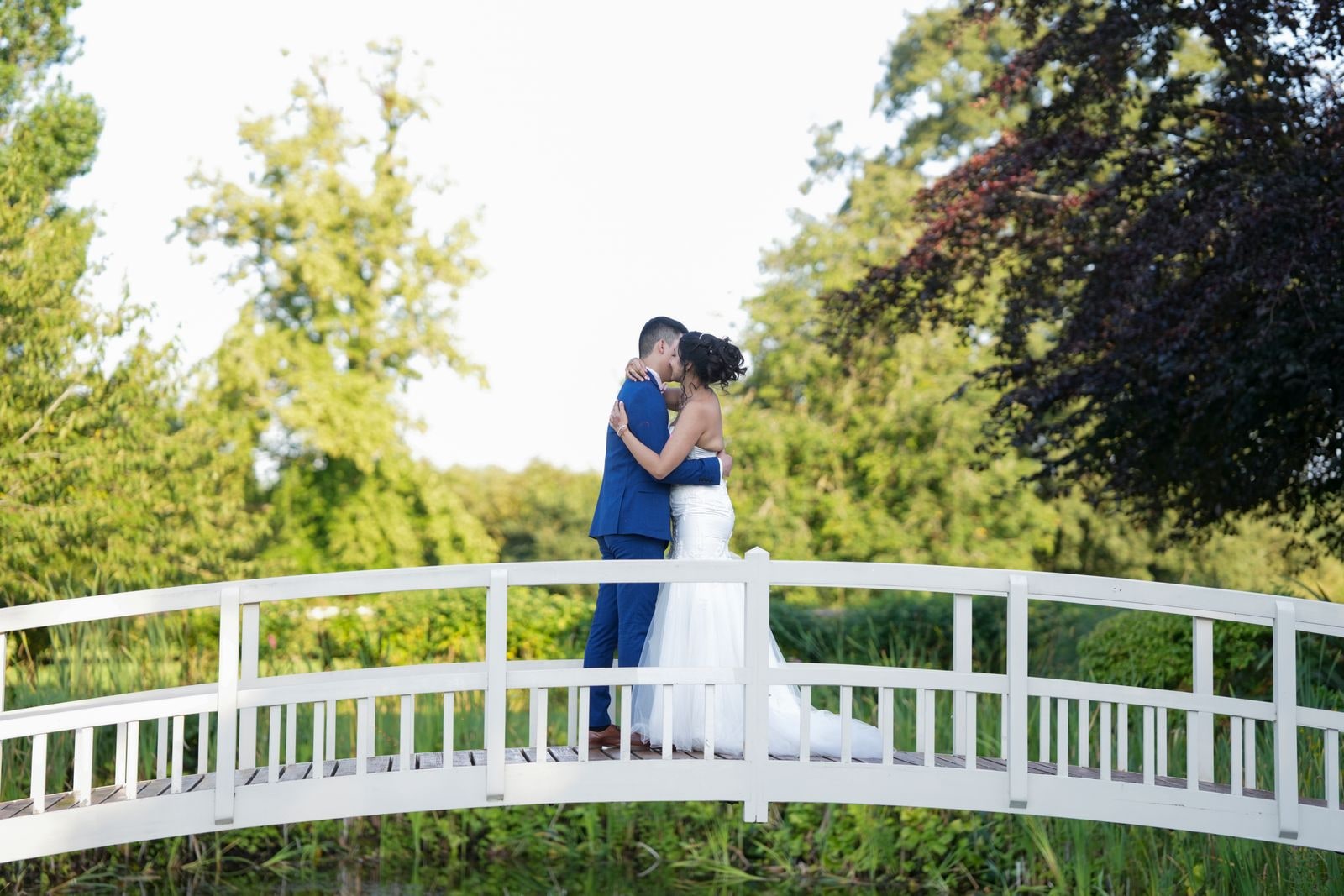 Couple kissing on the white arched footbridge, seen from below against the sky
