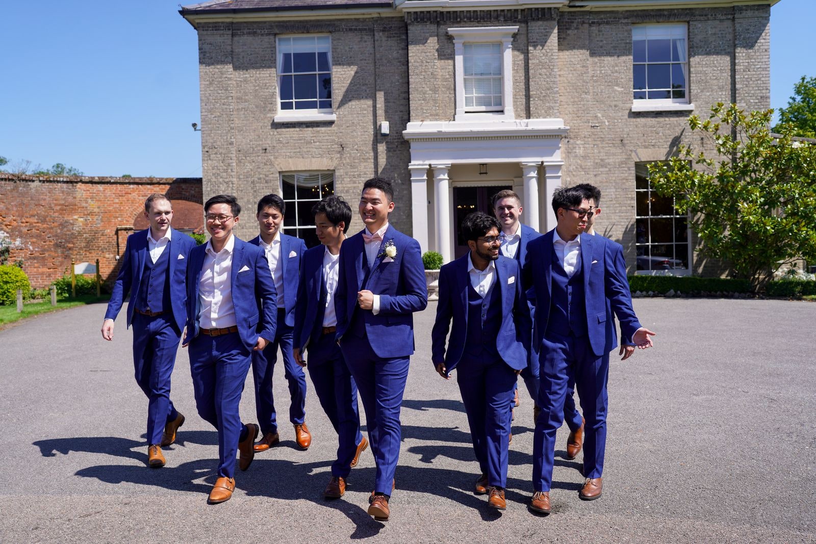 The groomsmen in blue three piece suits walking together across the drive