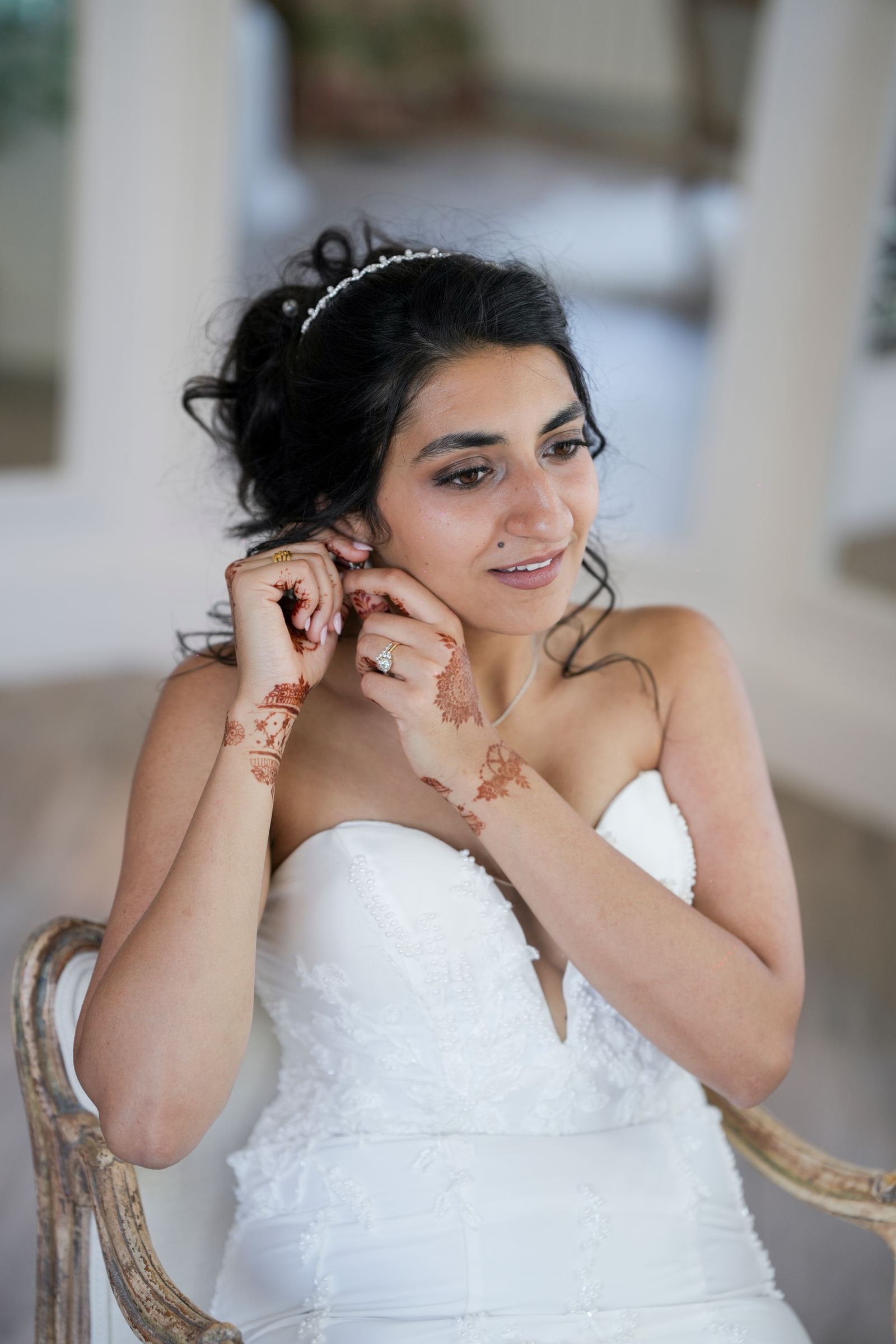Bride fastening her earring, her hands hennaed, seated in a gilt chair