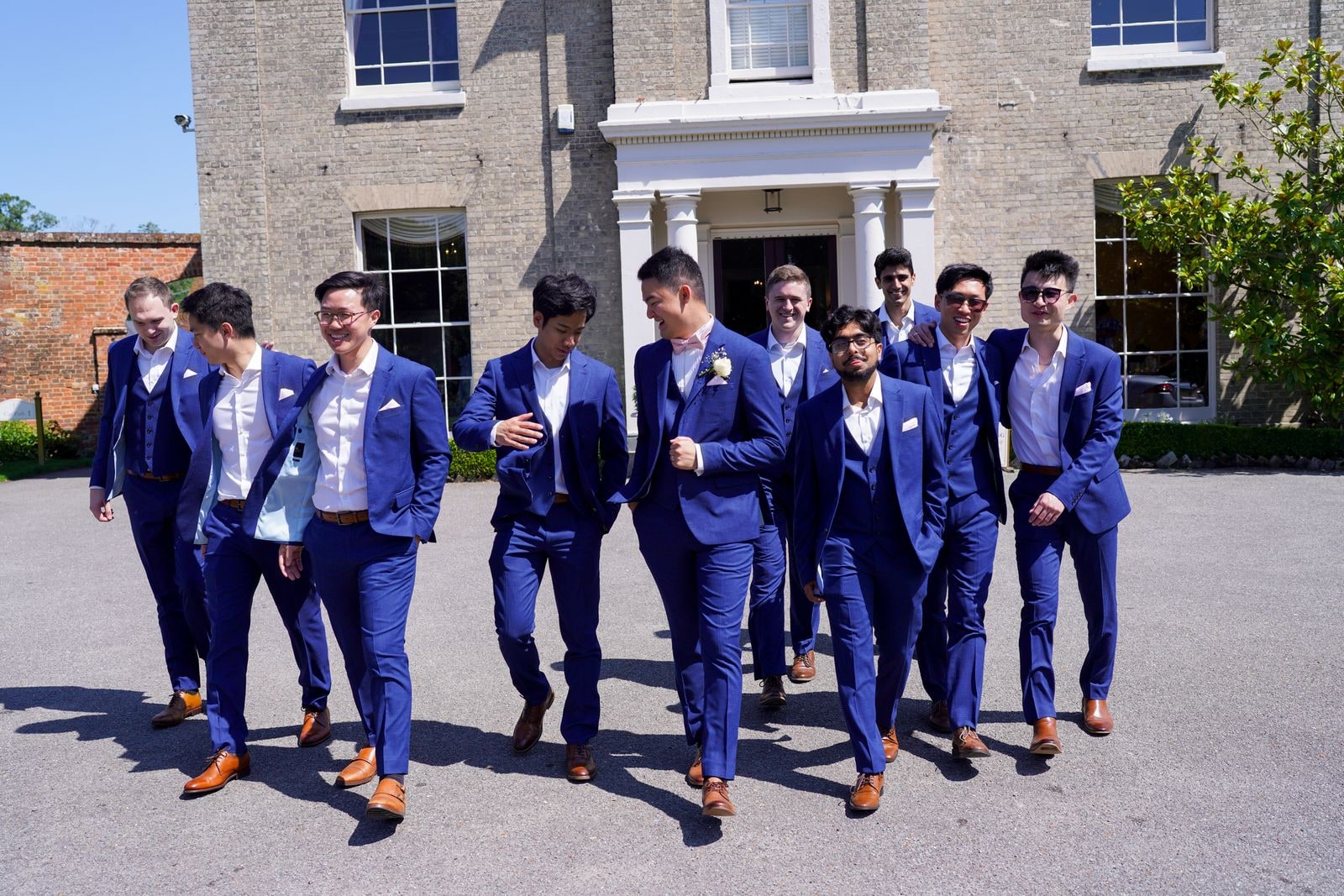 Groom and his groomsmen striding across the gravel in blue suits, the house behind them