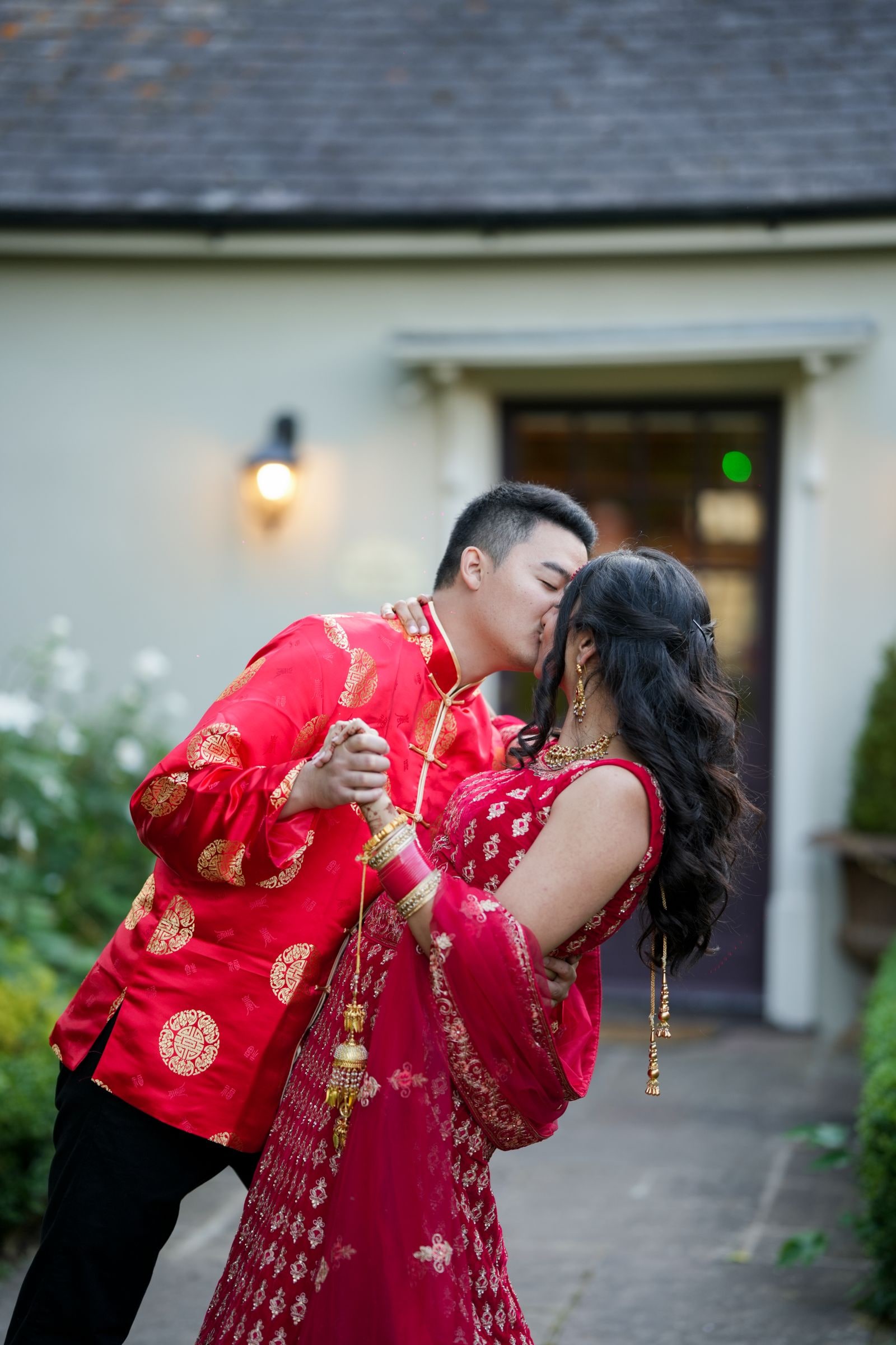 Couple in red and gold outfits, the groom dipping his bride outside the doorway