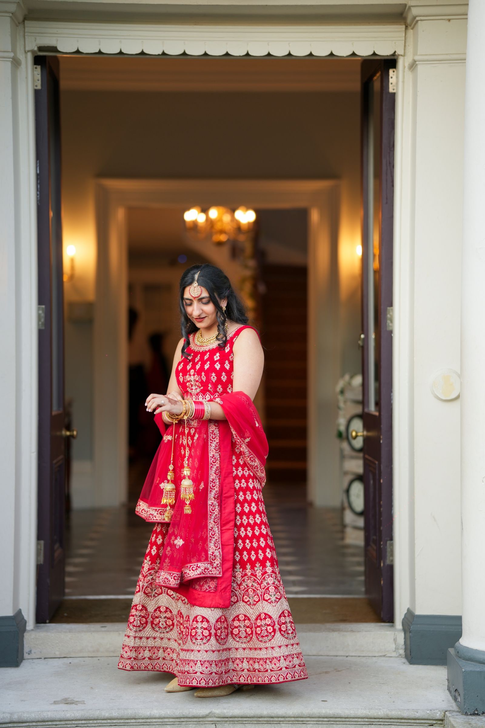 Bride in a red and gold lehenga standing alone in an open doorway