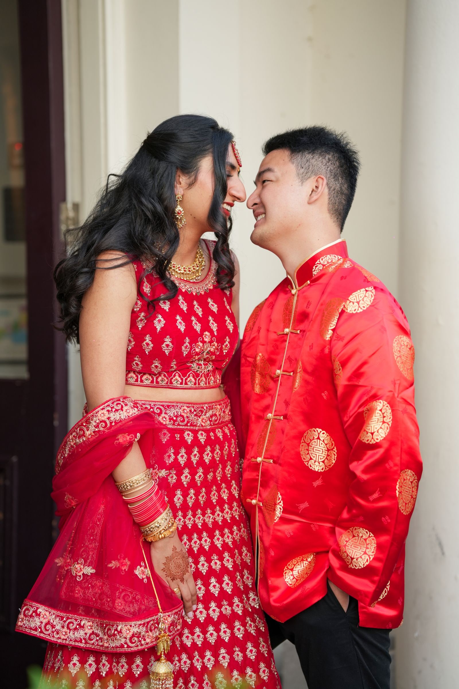 Couple face to face in matching red and gold, laughing between the pillars