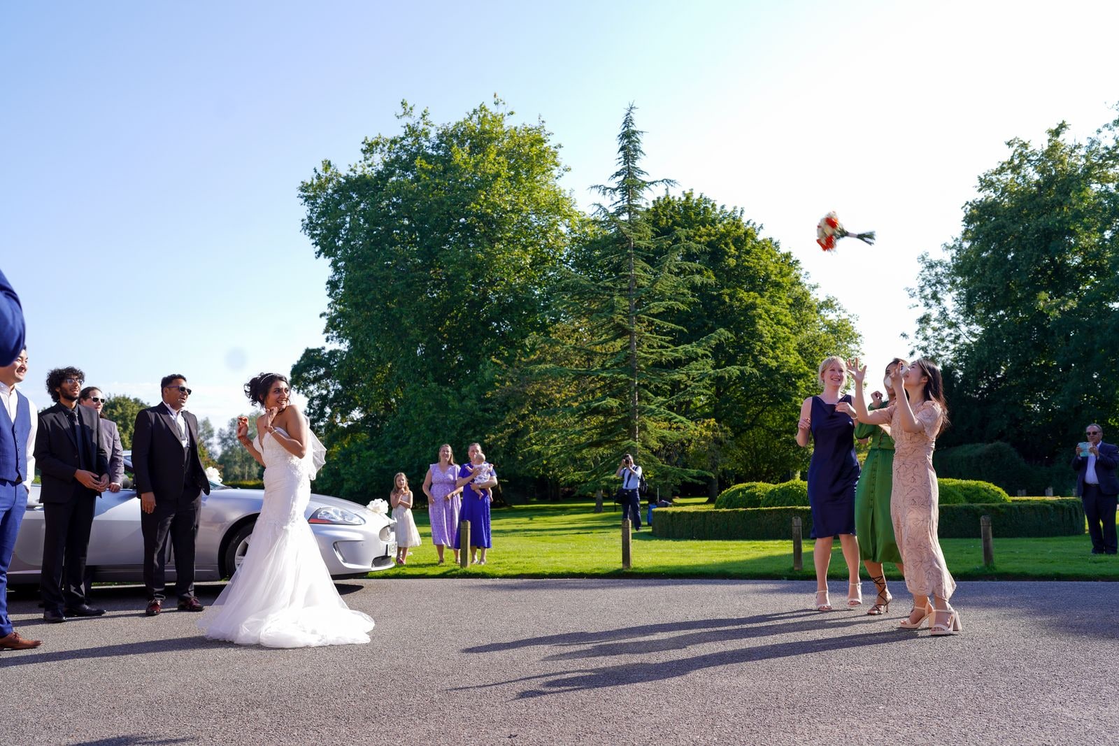 Bride throwing her bouquet over her shoulder as guests reach for it on the drive