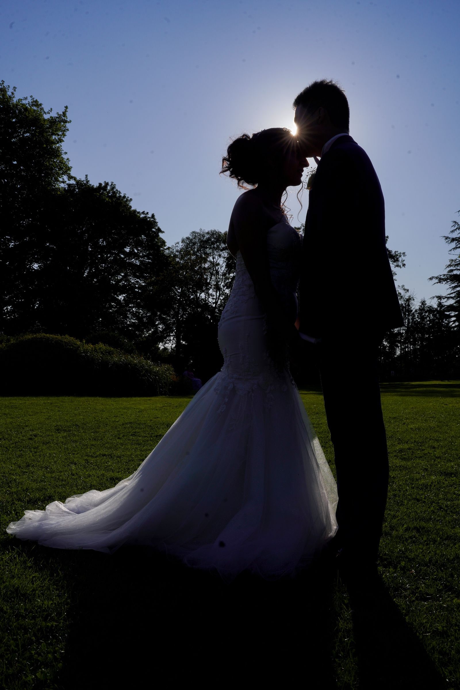 Bride and groom silhouetted against the setting sun on the lawn