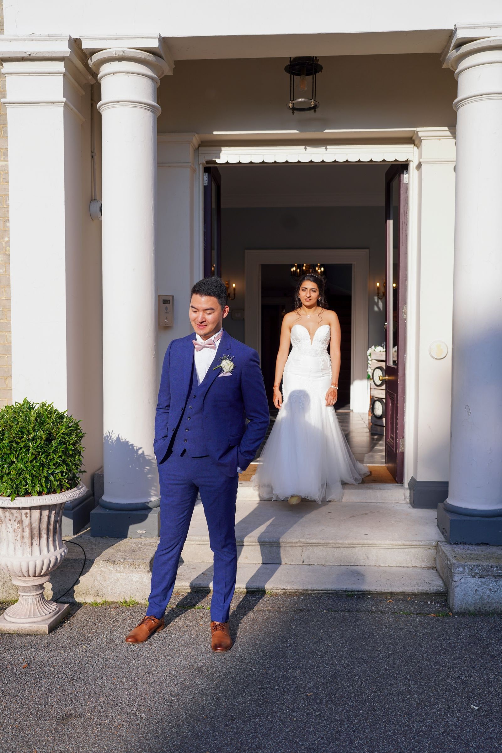 Groom waiting outside the pillared entrance as his bride comes through the doorway behind him