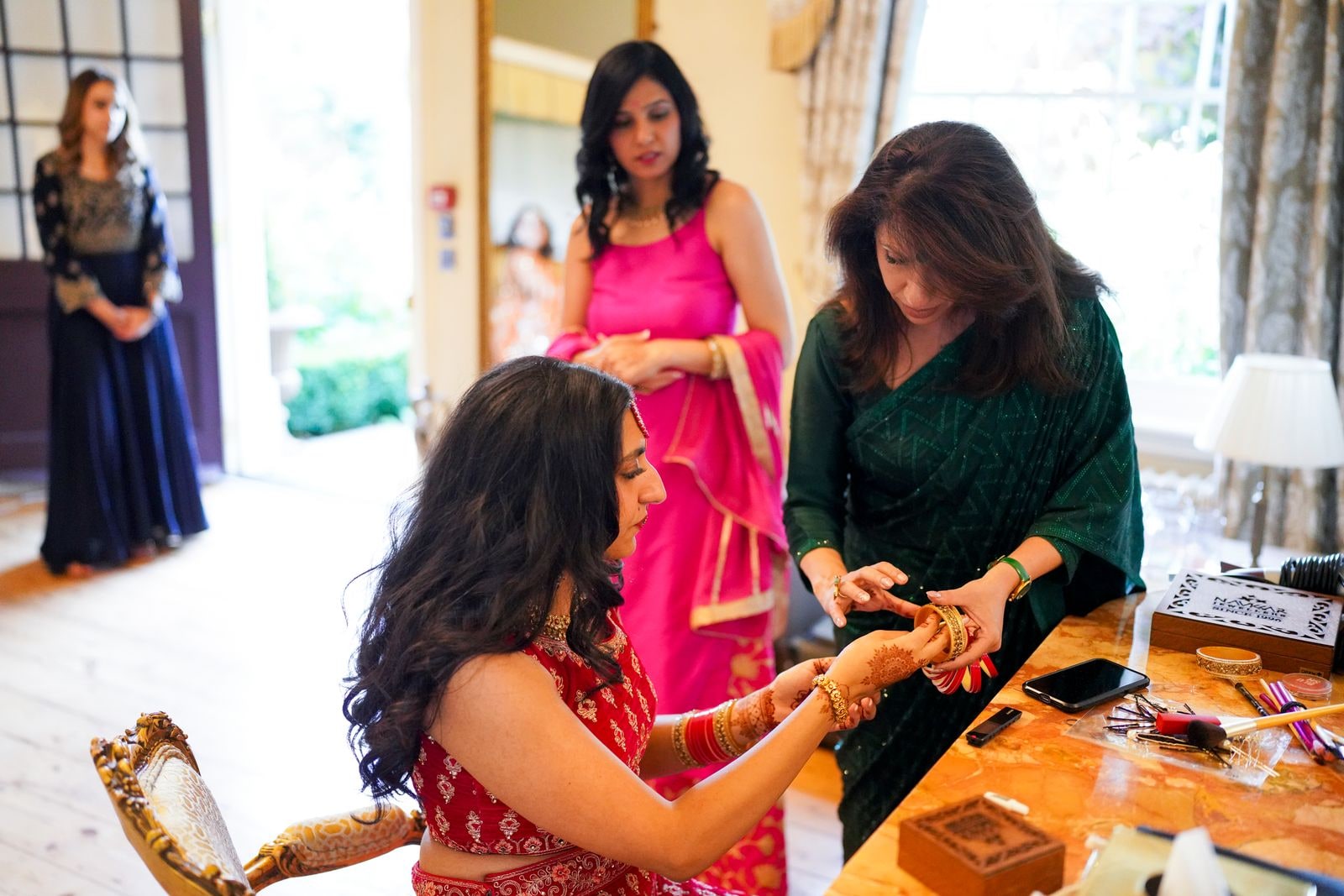 Bride having her bangles put on before the ceremony, family gathered around her