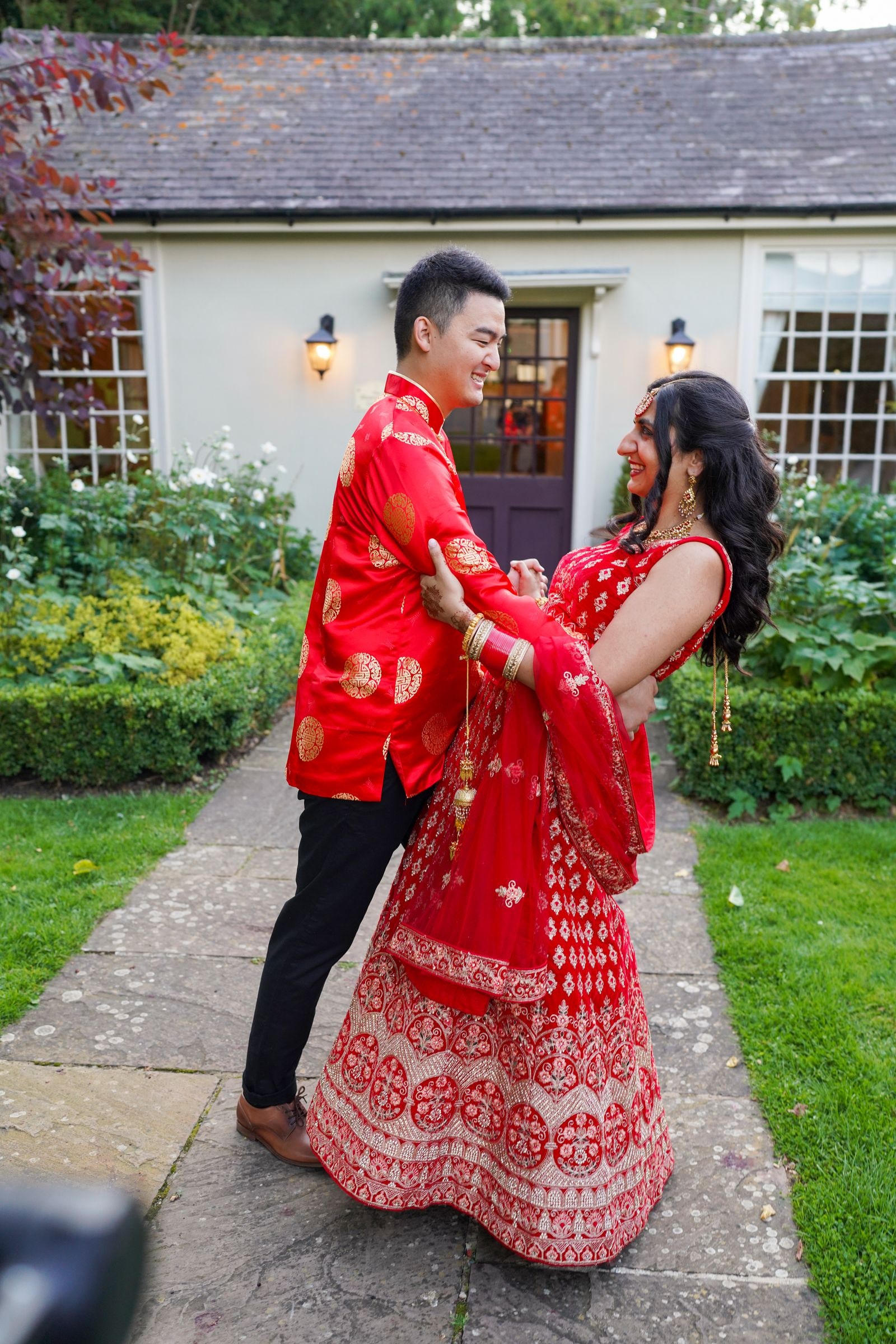 Groom spinning his bride on the garden path, her red lehenga flaring out