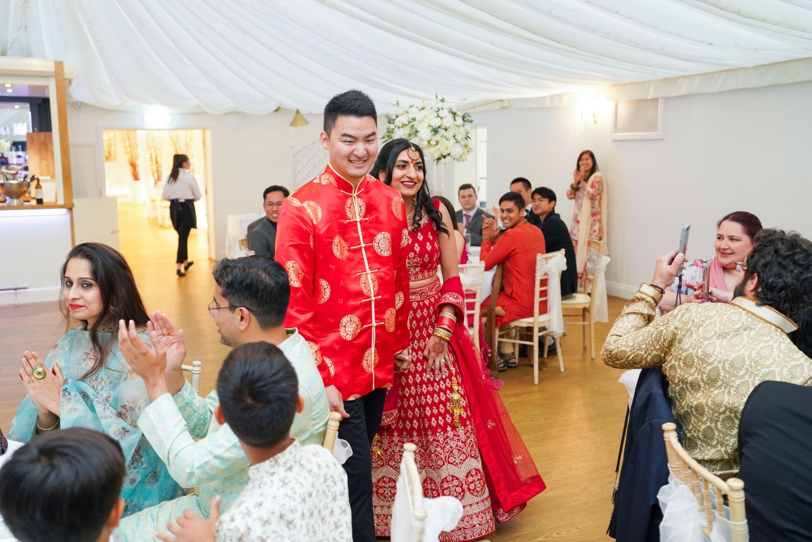 Guests applauding as the couple arrive into the marquee in red and gold
