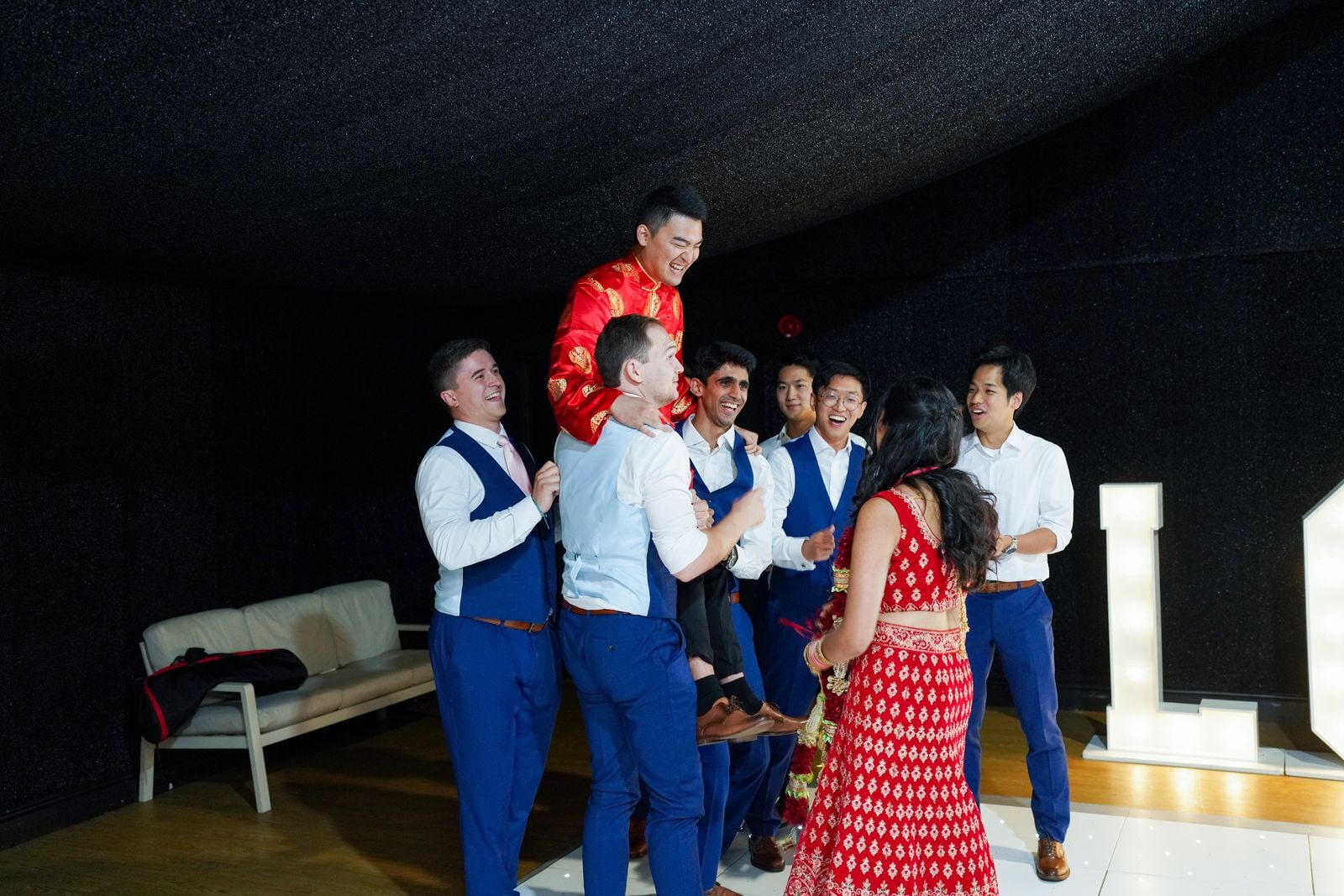 Groom being lifted by his friends on the dance floor, guests crowded round