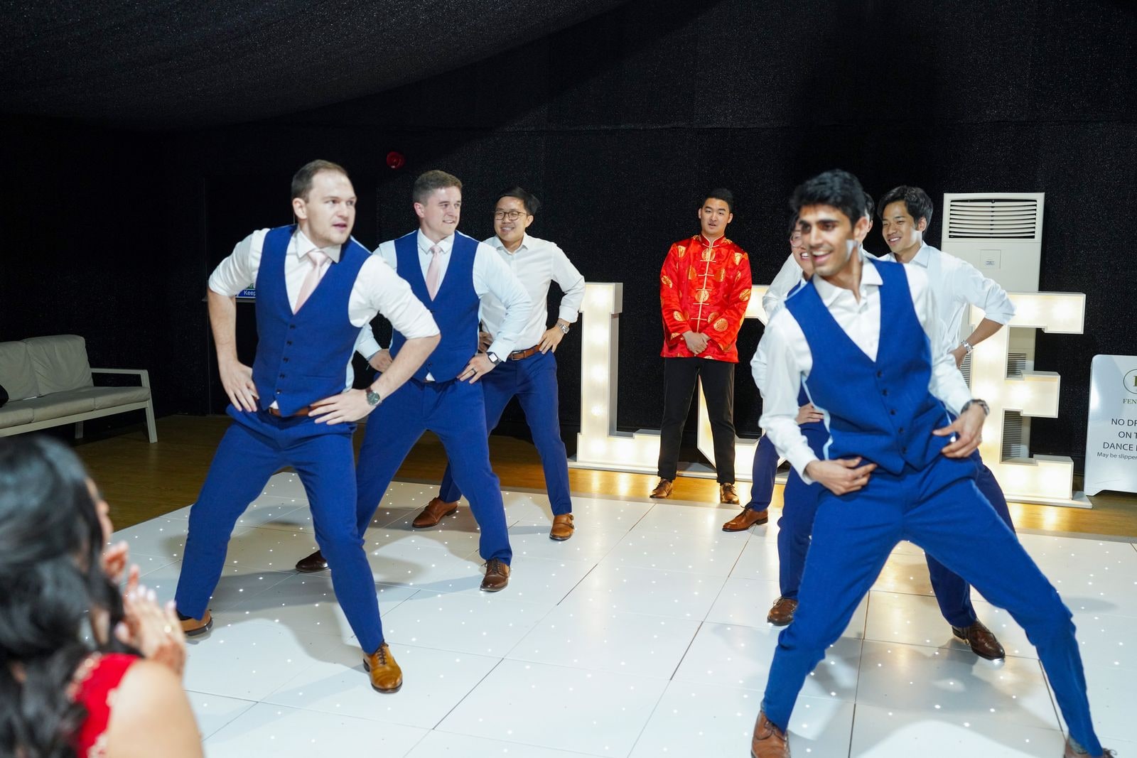 Guests in blue waistcoats performing a dance for the couple in front of the LOVE letters