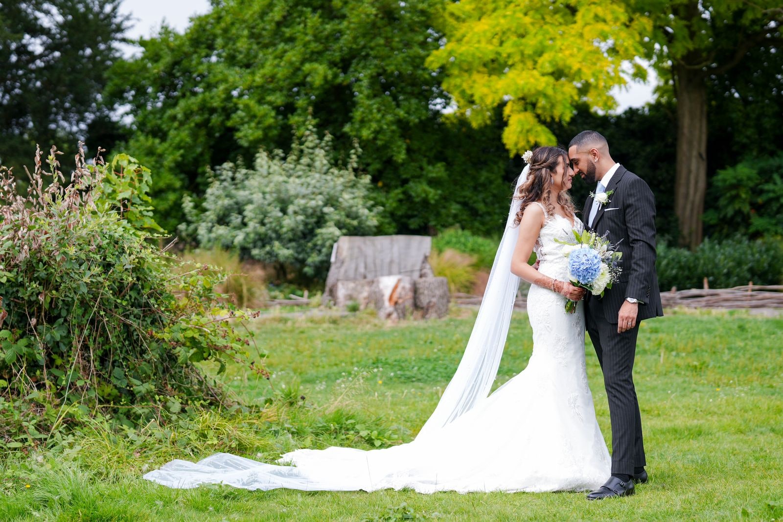 Bride and groom forehead to forehead in the garden, her long train across the grass
