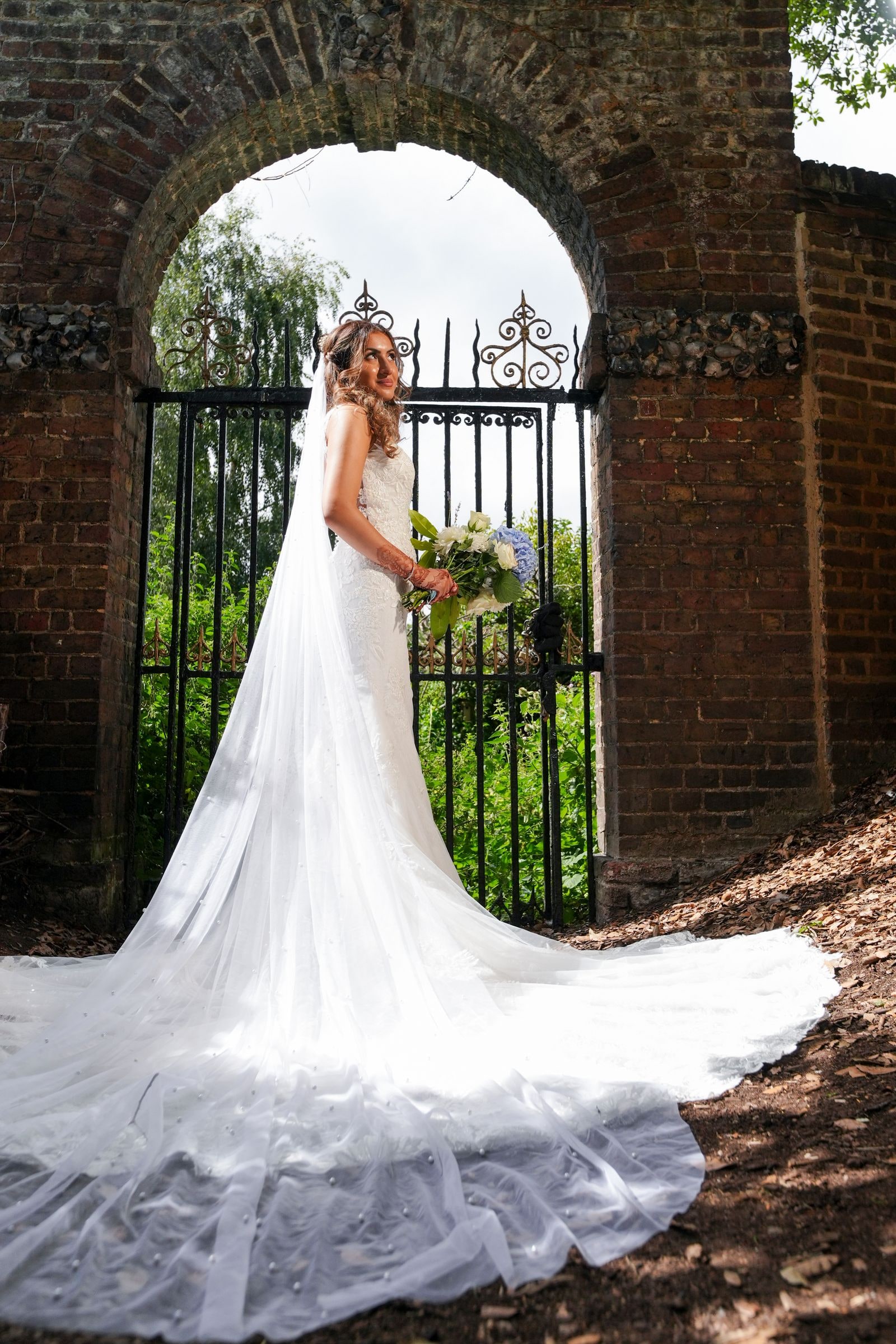Bride framed in a brick archway, her train spread across the ground