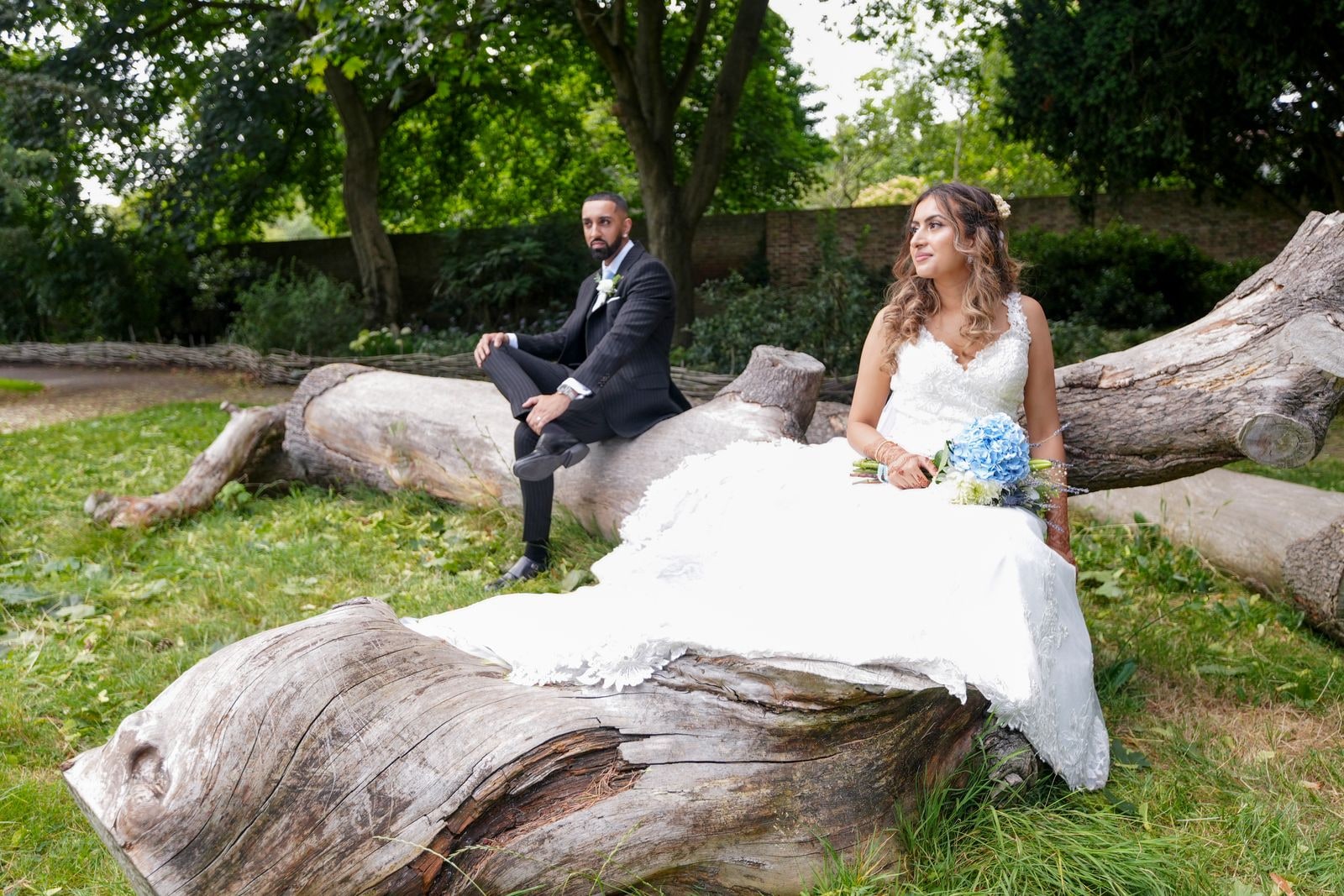 Bride and groom seated on fallen logs, her dress spilling over the wood