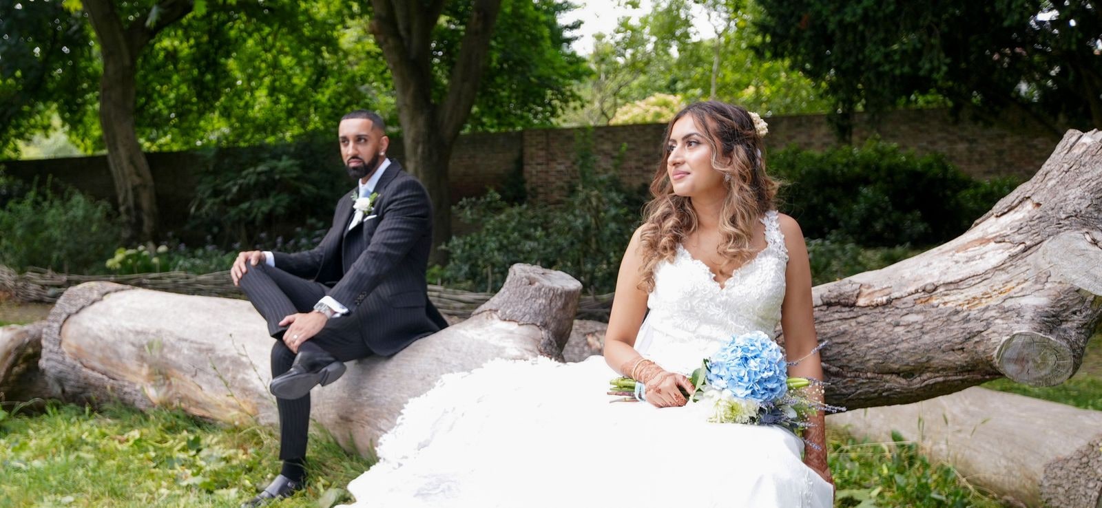 Bride and groom seated on fallen logs, her dress spilling over the wood